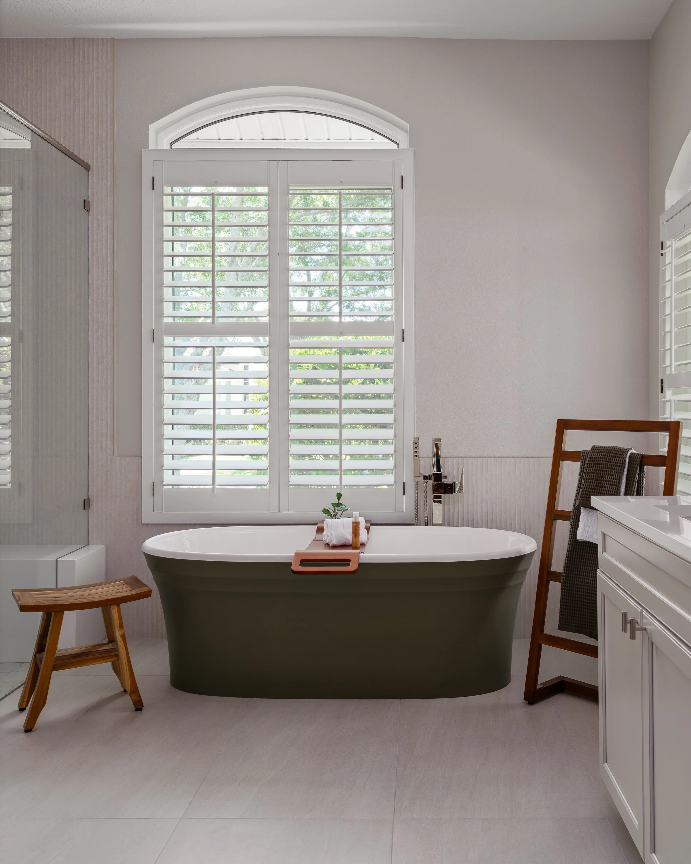 The olive-skirted acrylic freestanding tub in an asymmetrical bathroom
