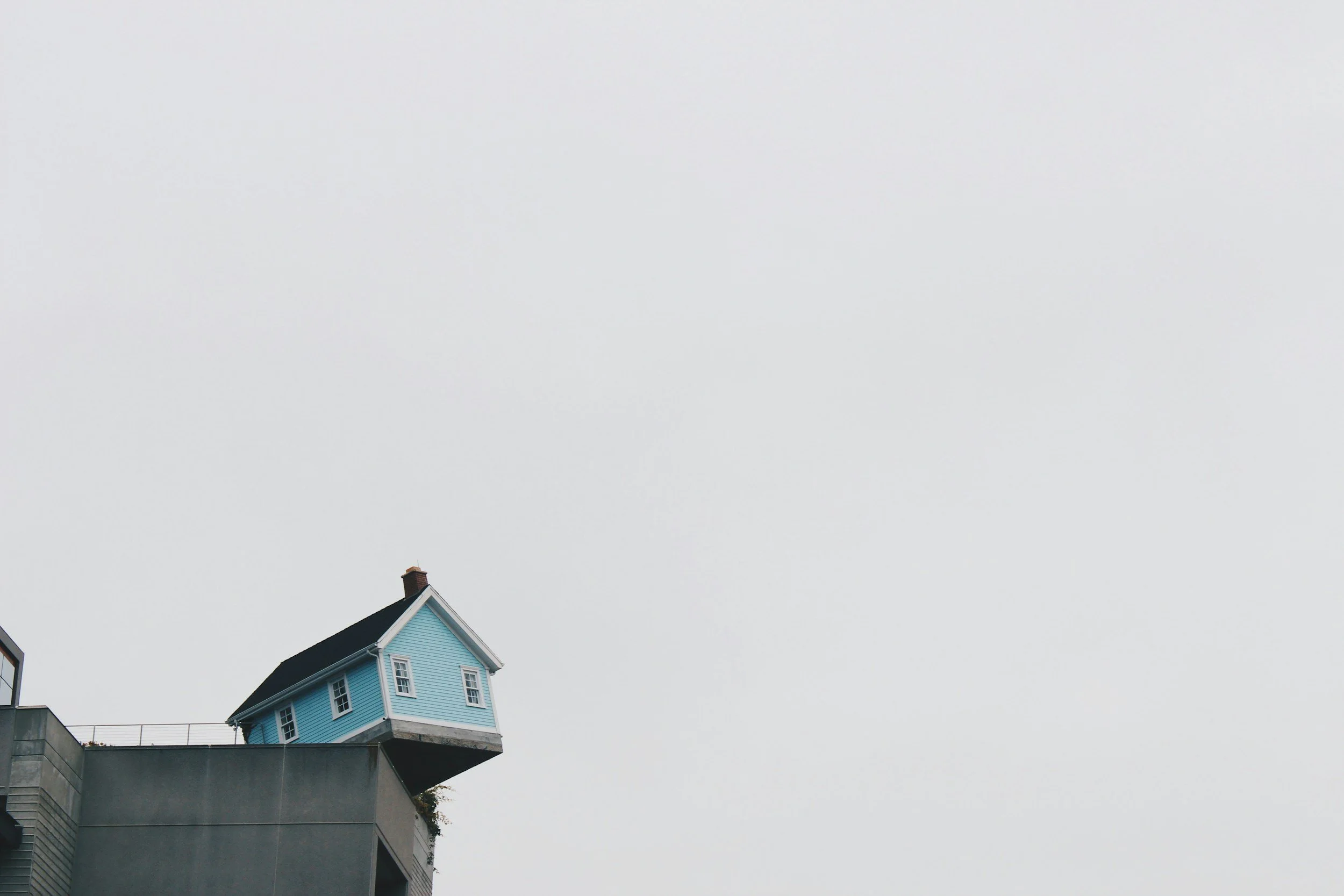 A blue house about to fall off of a concrete cliff