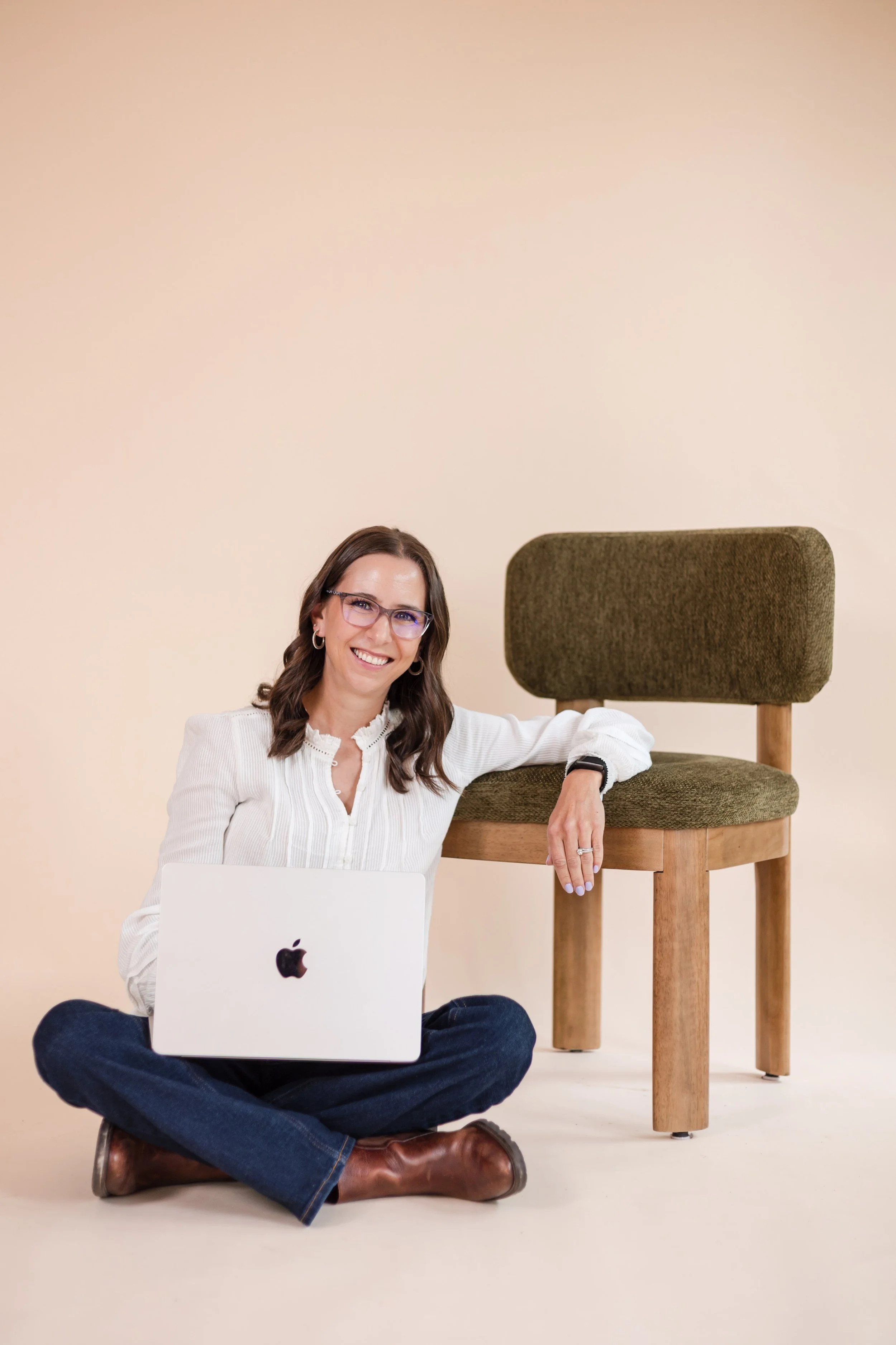 perinatal therapist brittany sallaberry sitting on floor with laptop and arm resting on green chair