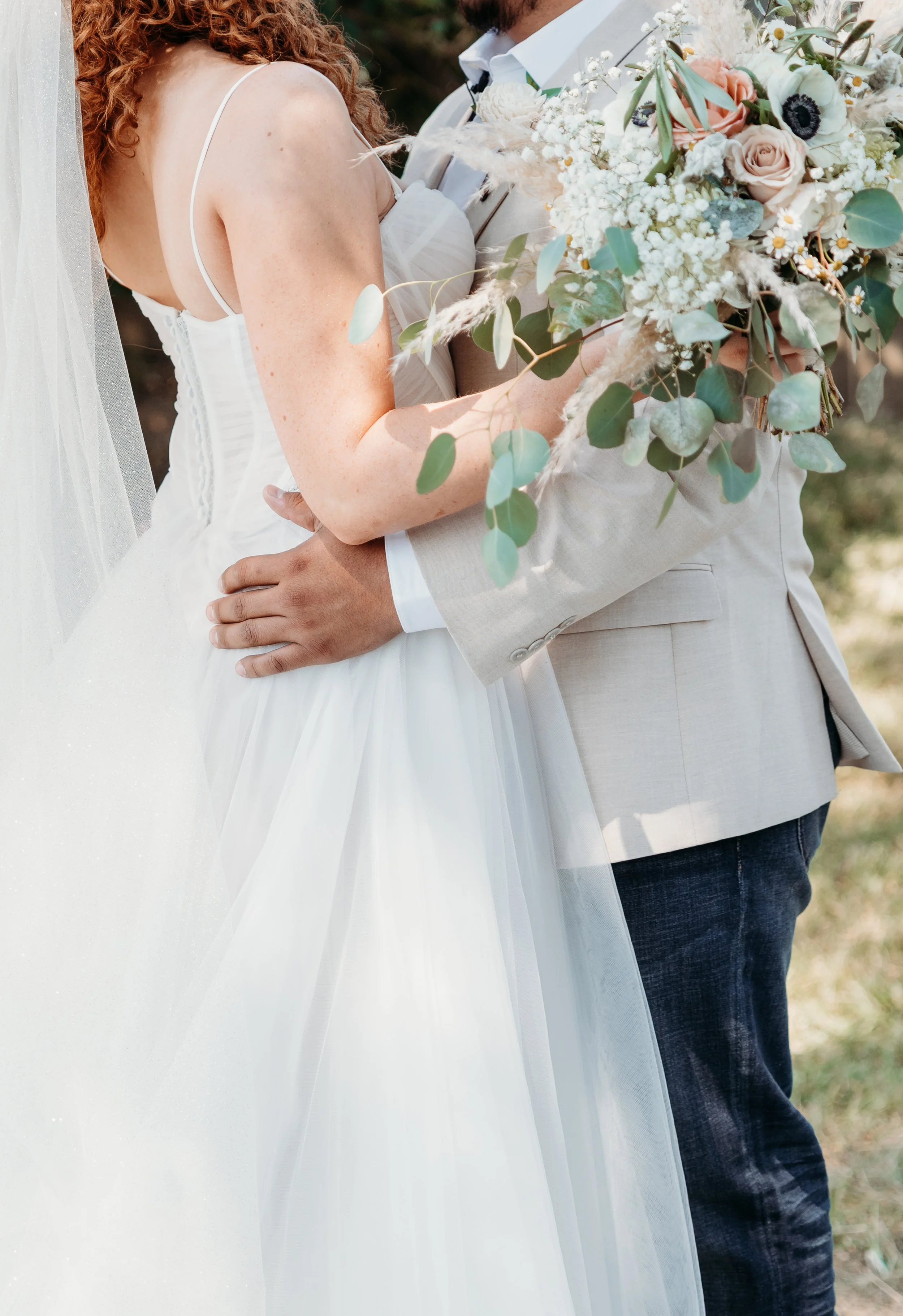 Close-up of a bride and groom embracing at their wedding, with the bride holding a bouquet of flowers.