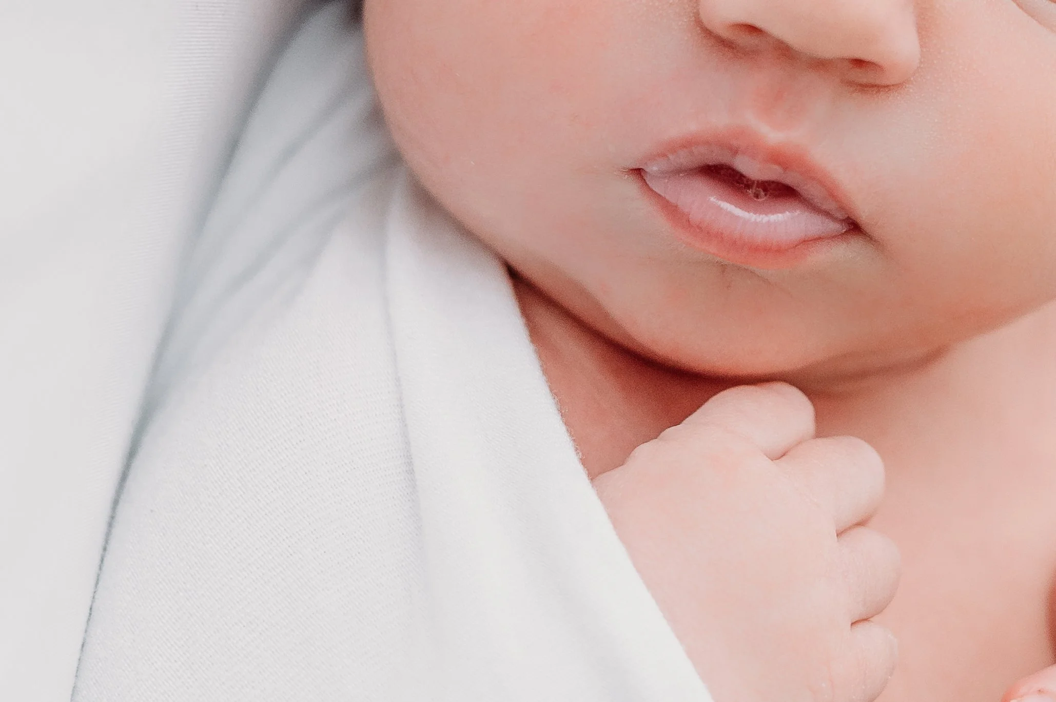 Close-up of a baby's face and hand, with the baby gently touching their chin and mouth slightly open.
