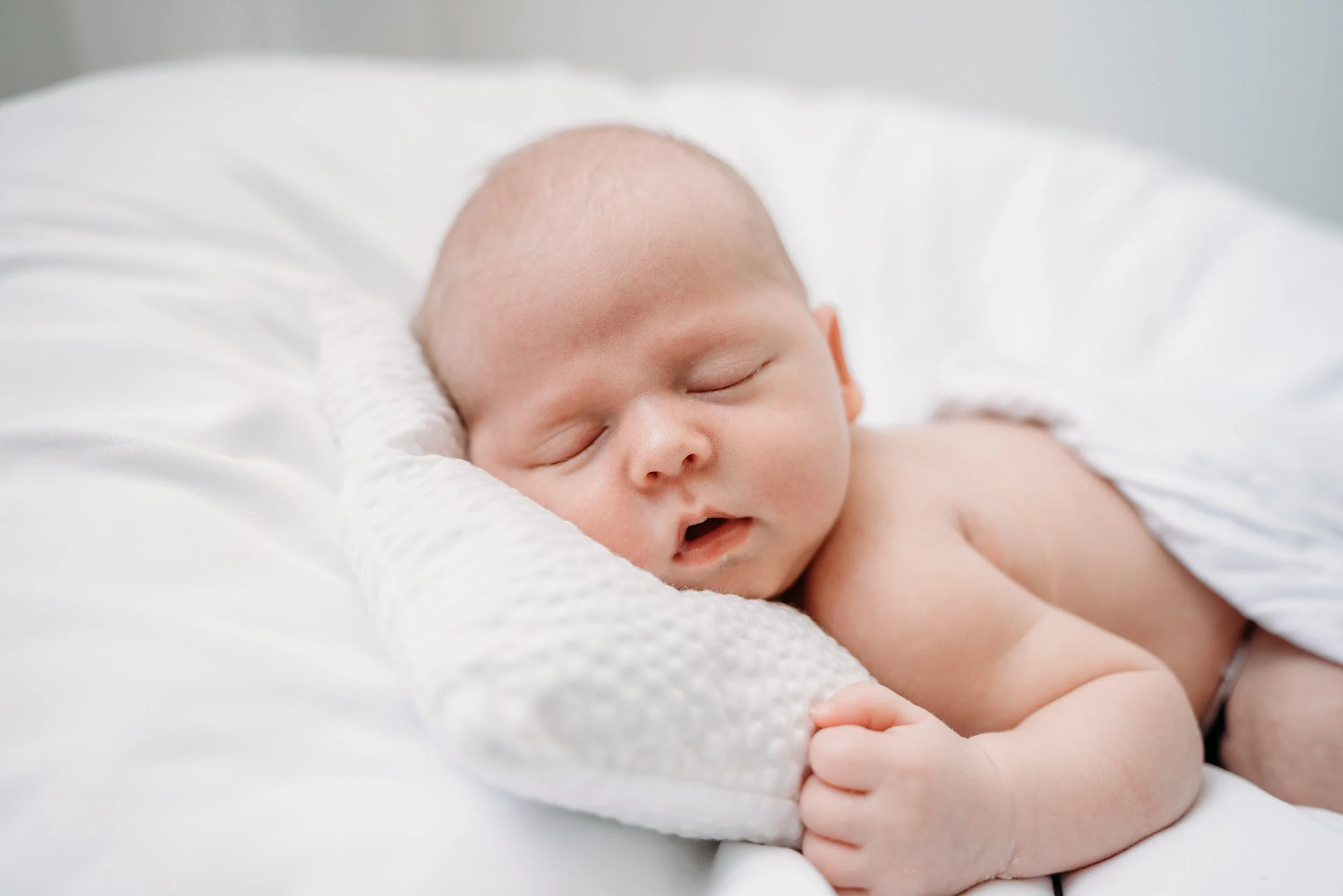 Close-up of a sleeping baby lying on a white bed with a textured white pillow.