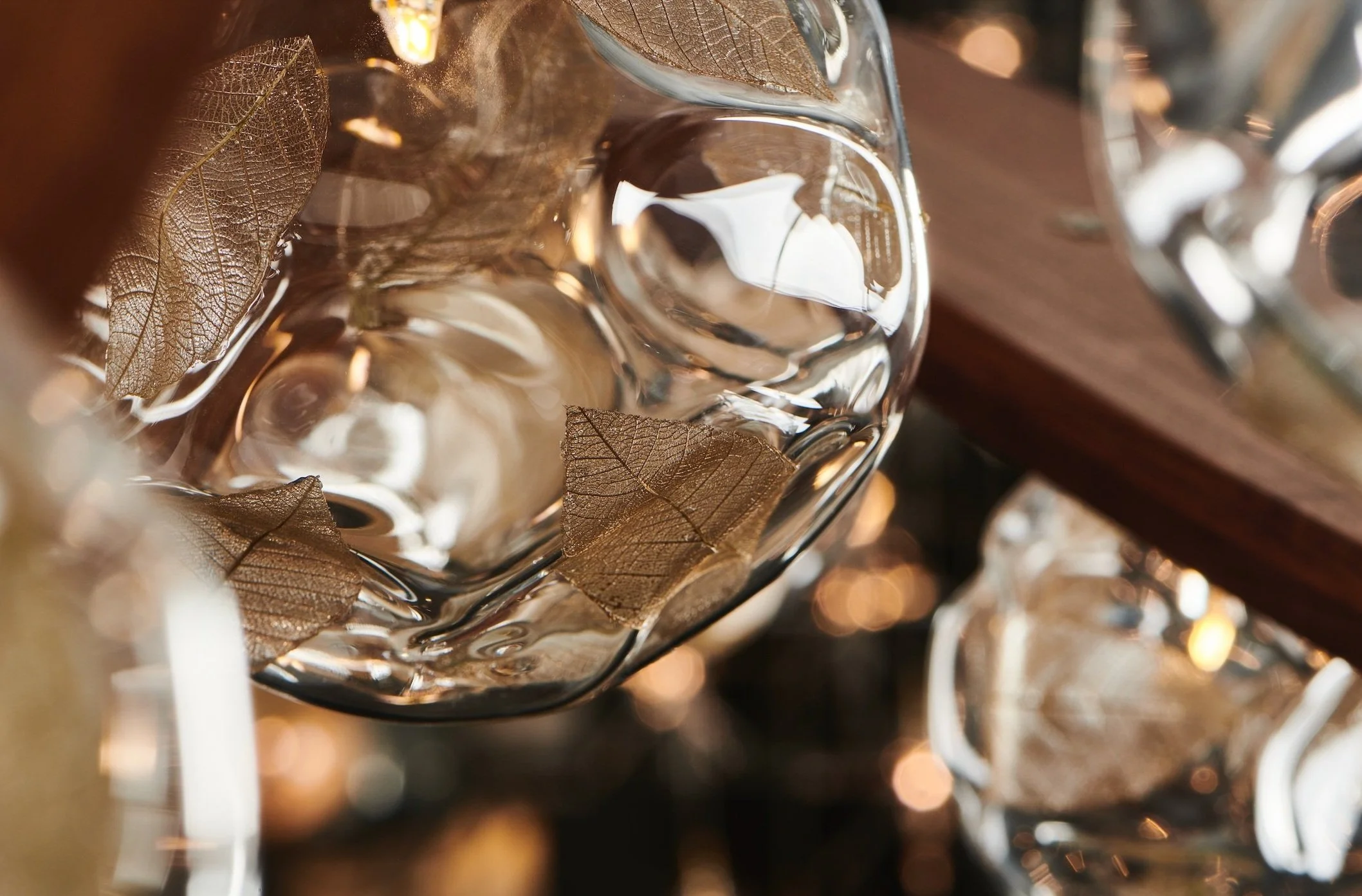 Close-up of a glass bowl with dried leaves inside, reflecting light and creating a warm glow.