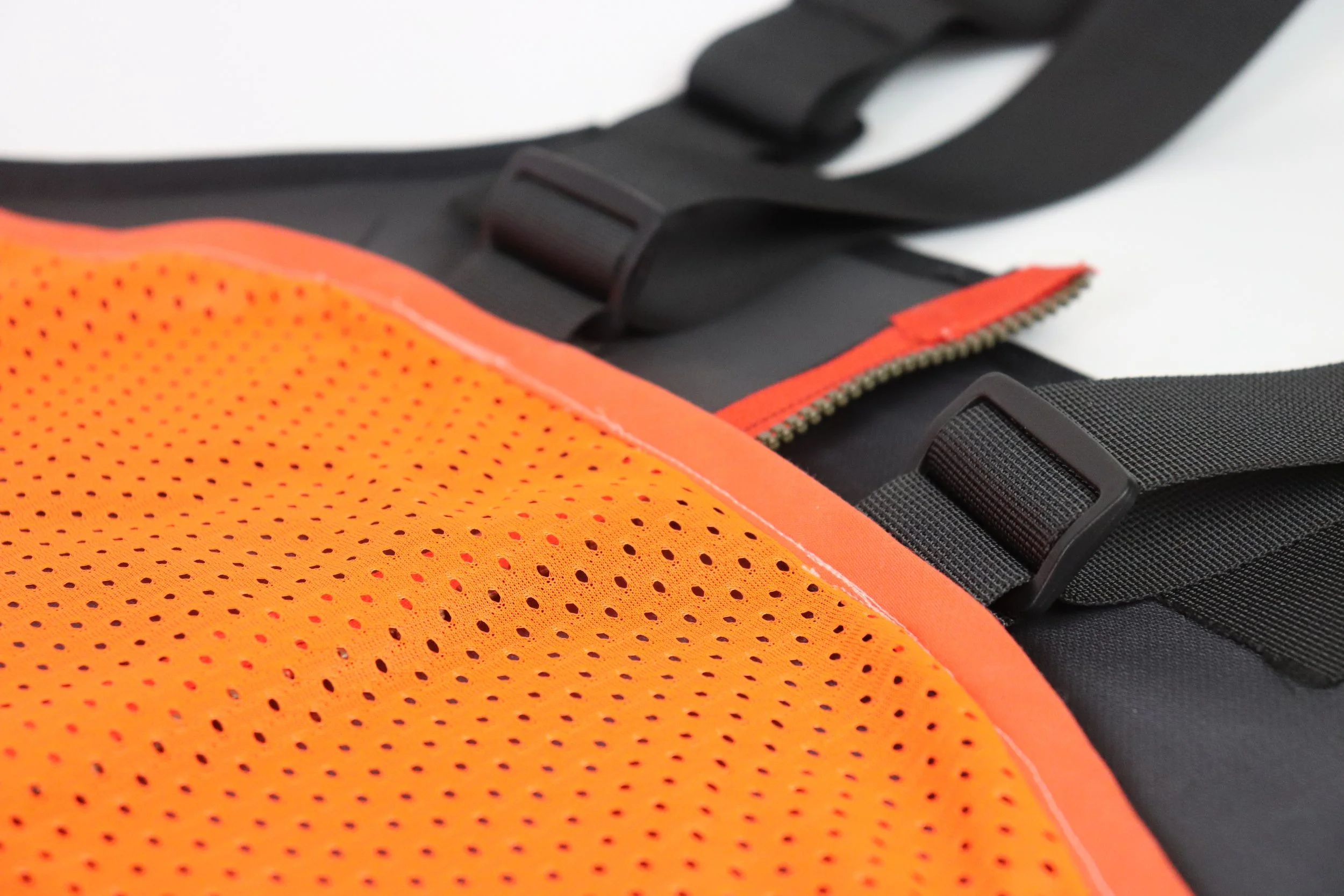 Close-up of a black backpack with orange reflective accents and an orange mesh pocket.