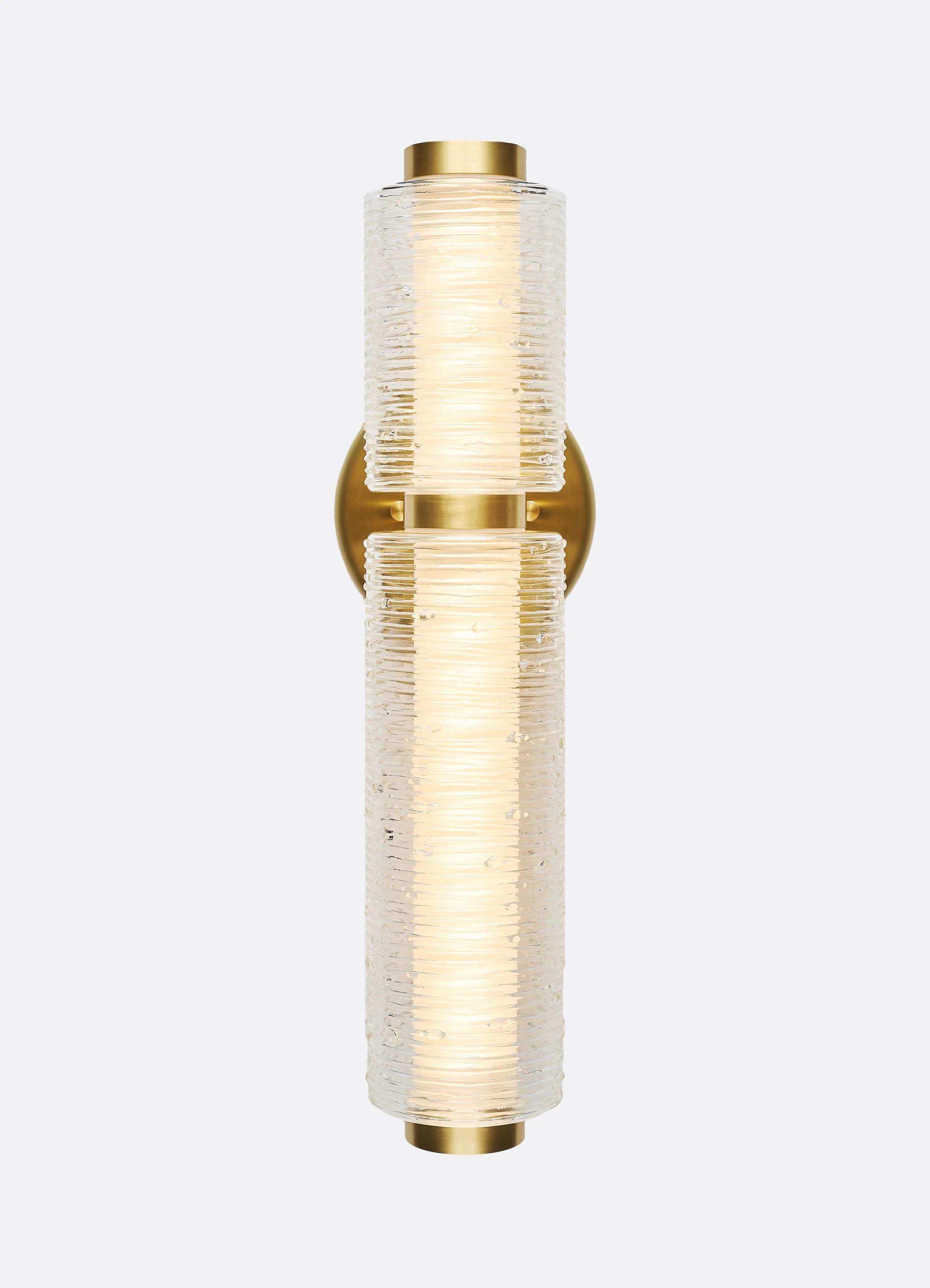 Wall-mounted light fixture with a clear textured glass shade and a gold metal base, illuminating in a bright white light.
