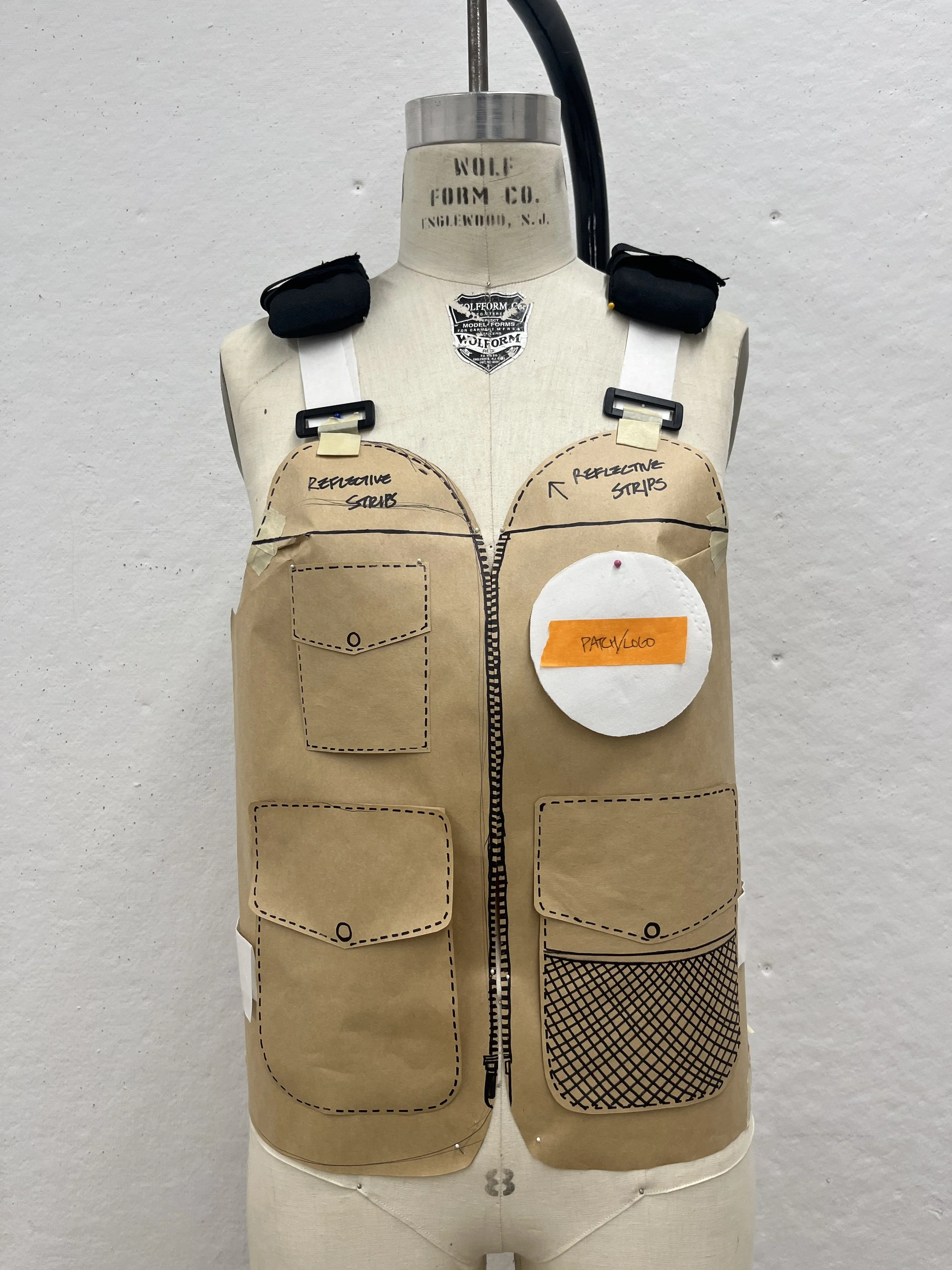 A dress form with paper pattern pieces attached, labeled with 'Reflective Strips' and 'Part Logo,' used for designing a construction vest.