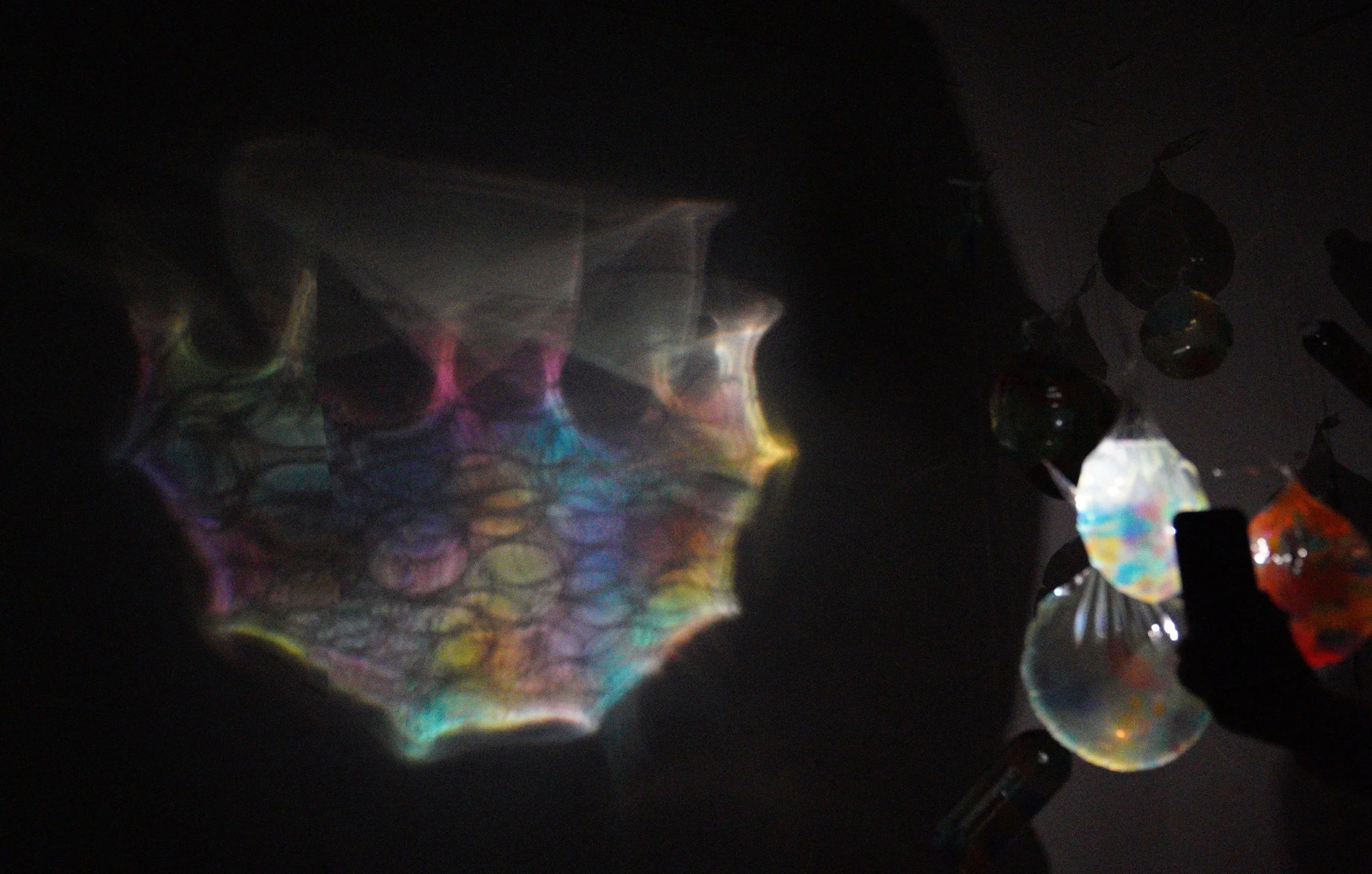 Dark background with reflections of colorful, iridescent objects, some resembling glass or crystals, and shiny black beads or stones.