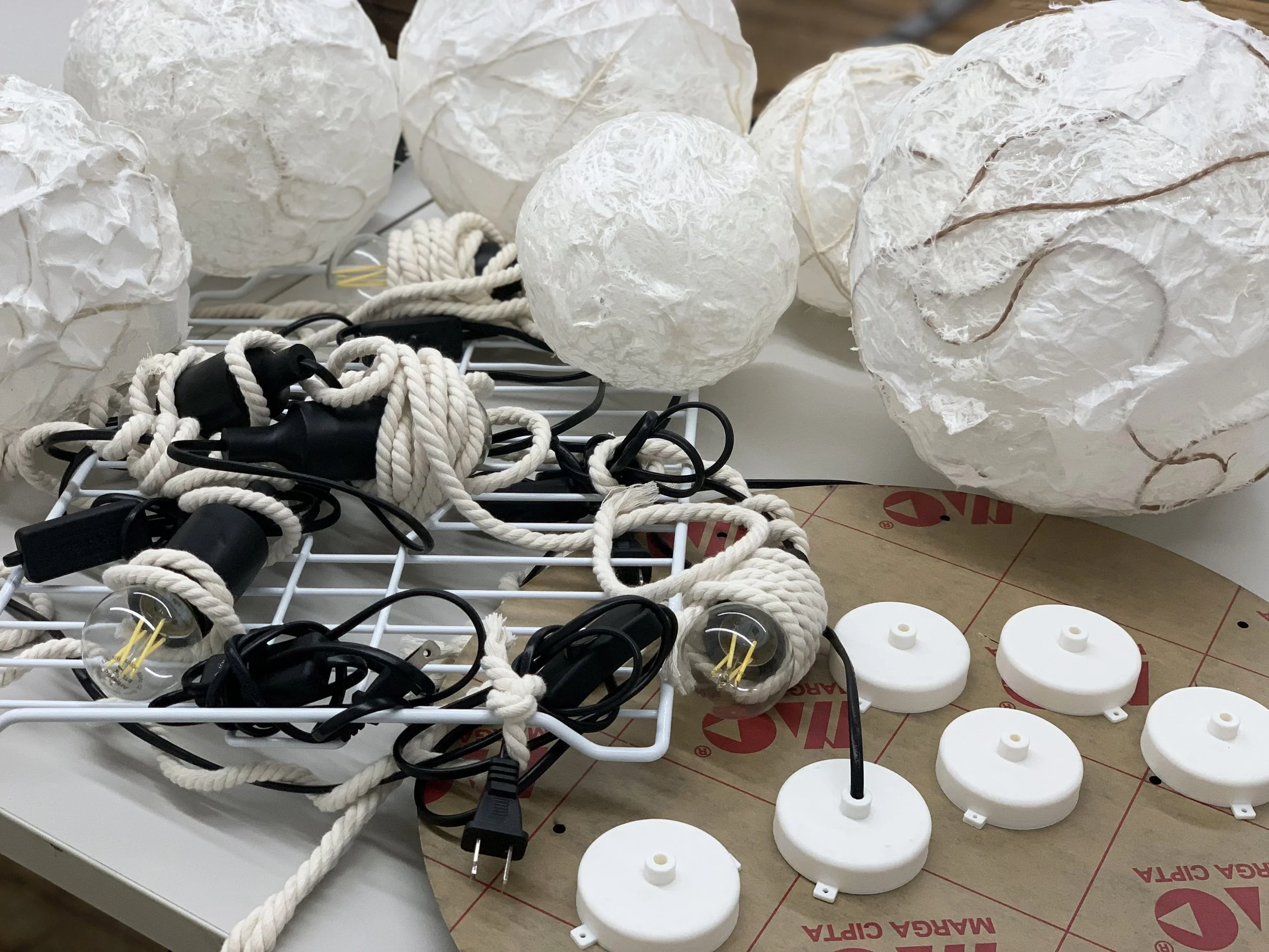 Unassembled string lights with tangled cords, white paper lanterns, and round white plastic mounts on a work surface.