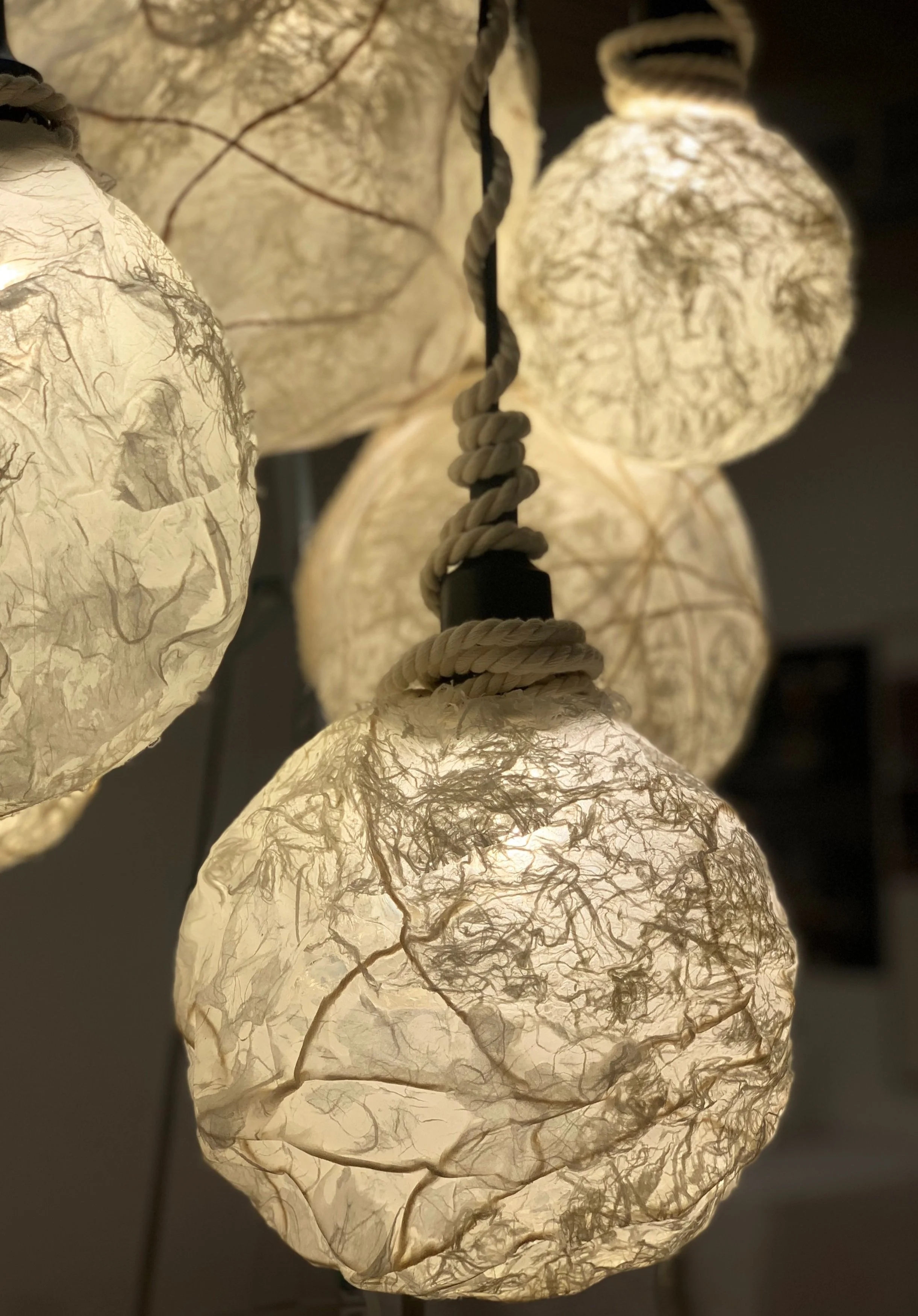Close-up of a hanging light fixture with multiple paper lanterns illuminated from within, connected by a twisted cord.