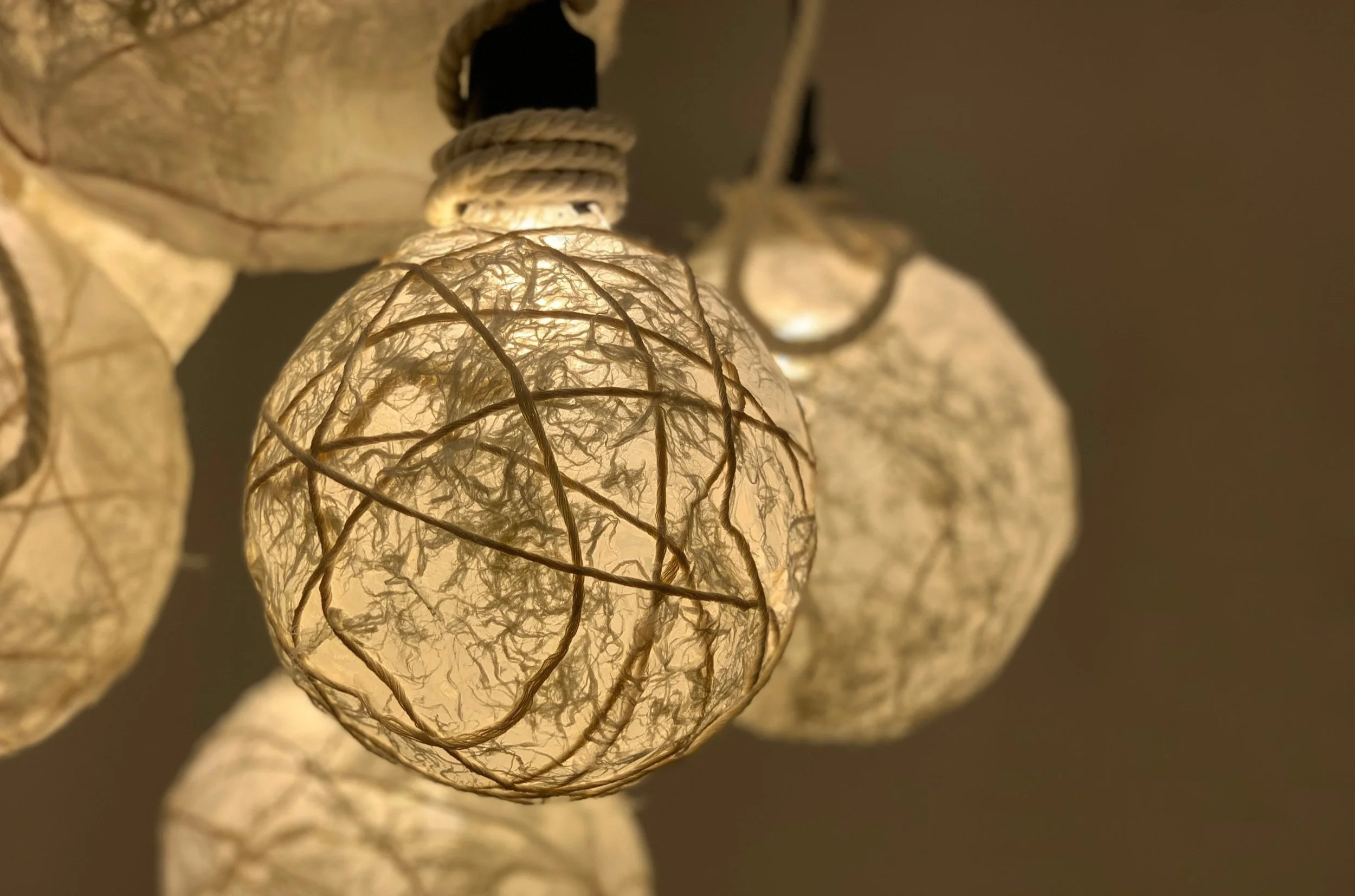 Close-up of illuminated paper lanterns with a textured, crumpled paper appearance and thin wire framing, hanging against a dark background.