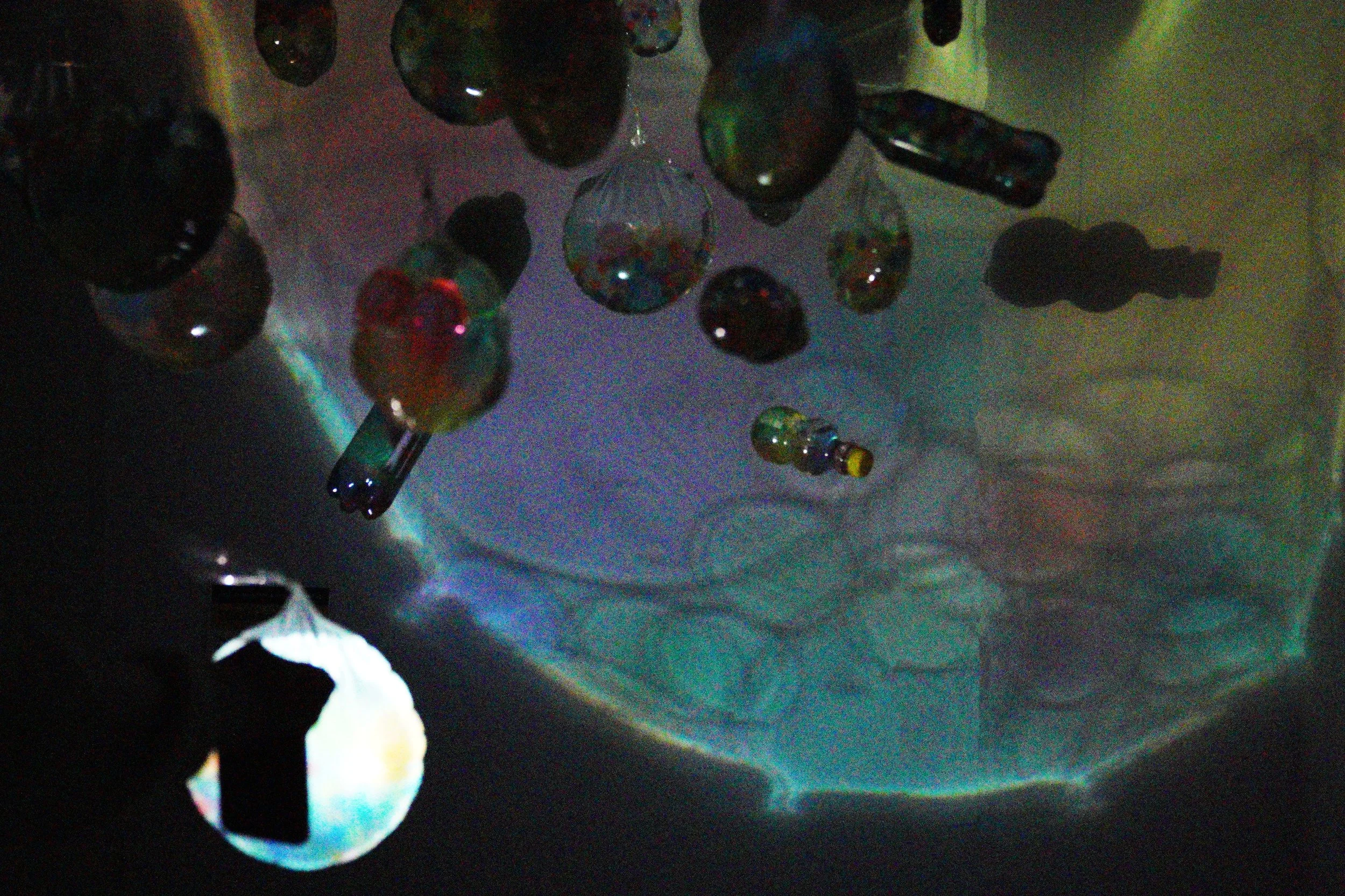 Colored glass marbles and a few small glass containers are hanging upside down, reflecting light onto a white surface.
