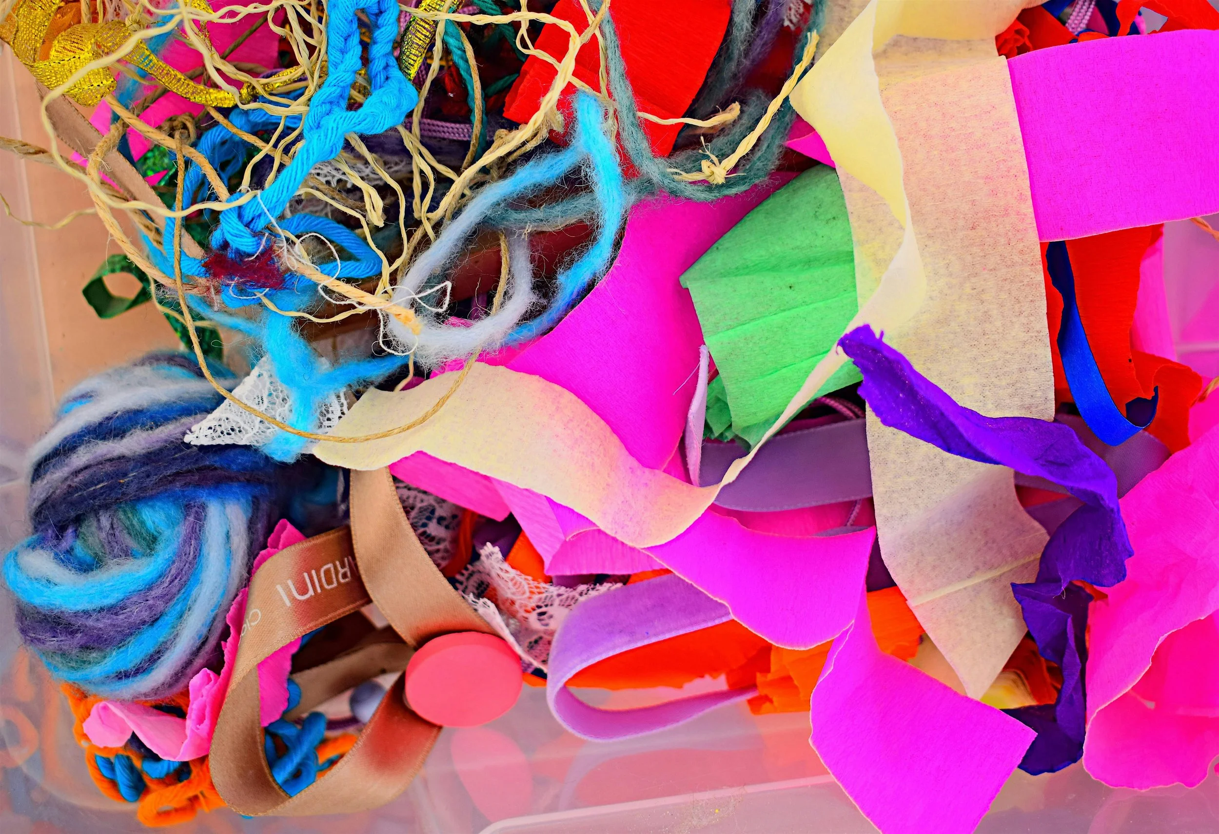A colorful assortment of craft materials including tissue paper, yarn, ribbons, and tulle in bright colors like pink, purple, green, blue, yellow, and red.