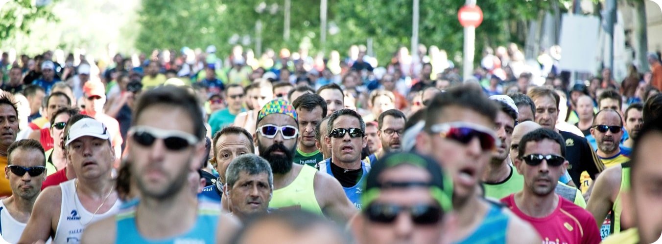 Crowd of runners wearing sports sunglasses and athletic gear participating in a marathon or race on a tree-lined street.