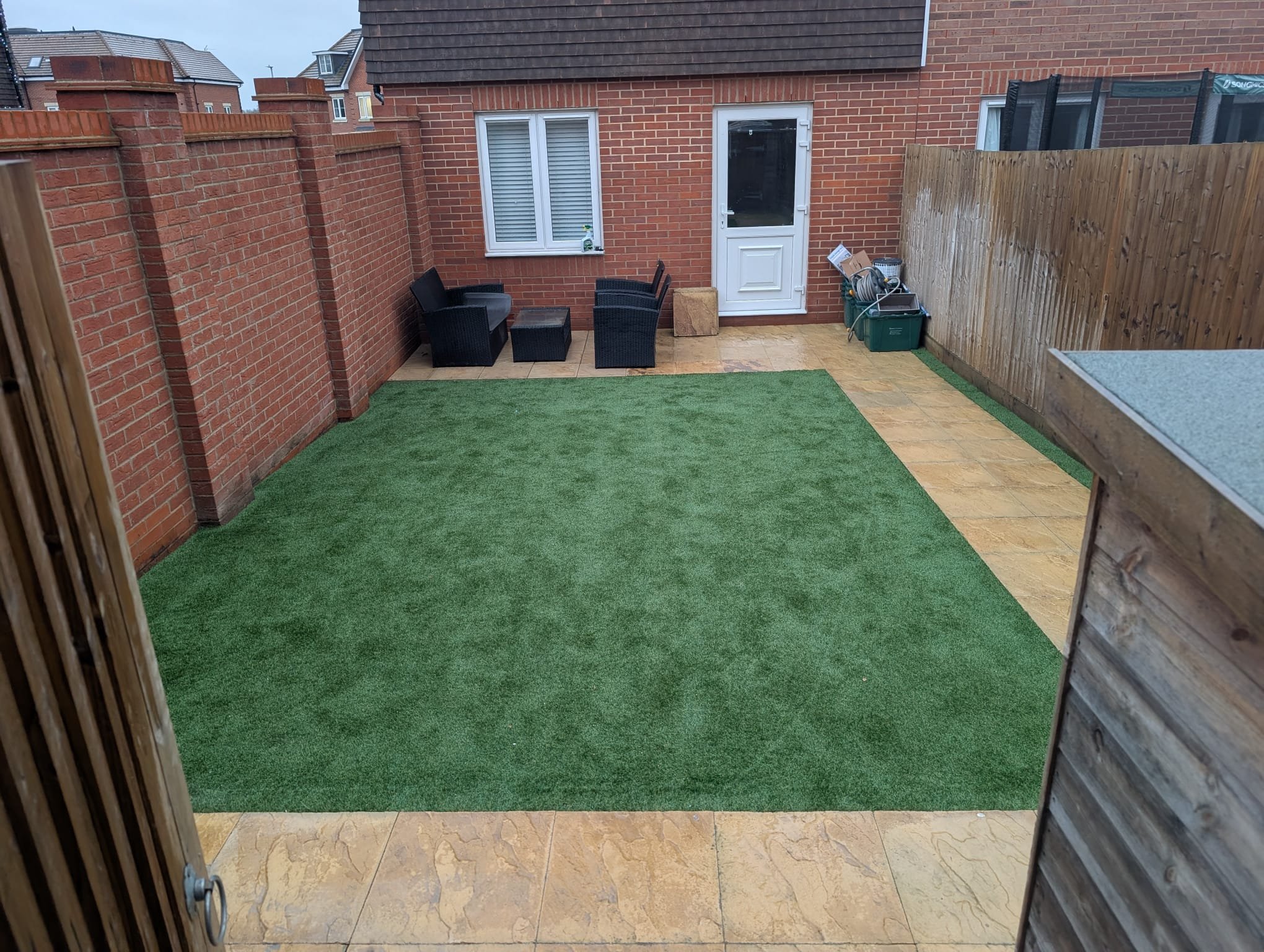 Backyard with artificial grass, potted furniture, and a brick wall.