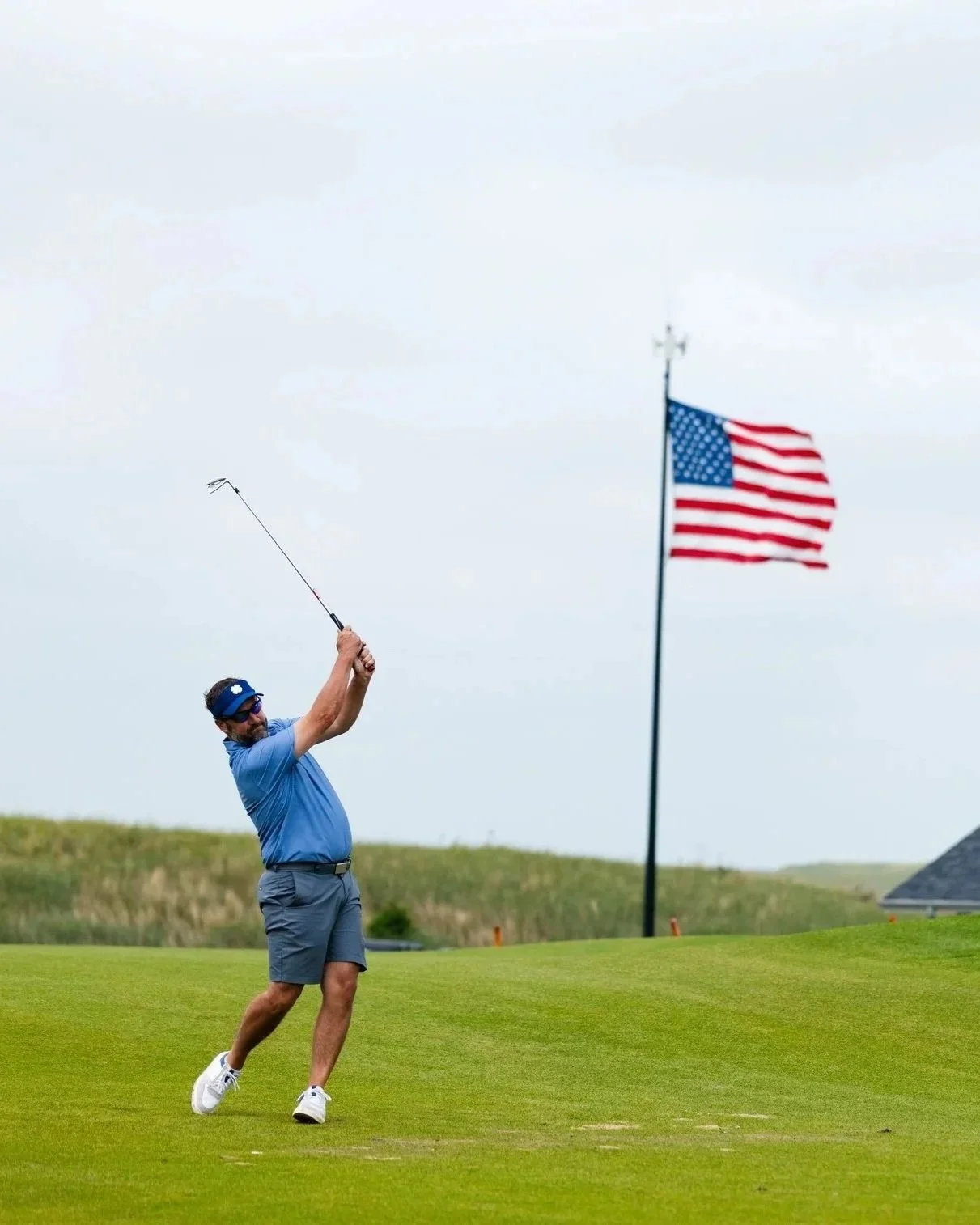 Man playing golf at GrayBull Club with a US Flag in the background