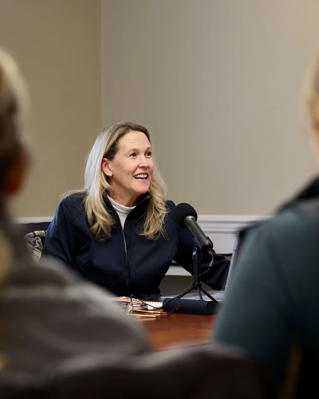 A woman with blonde hair speaking into a microphone during a meeting.
