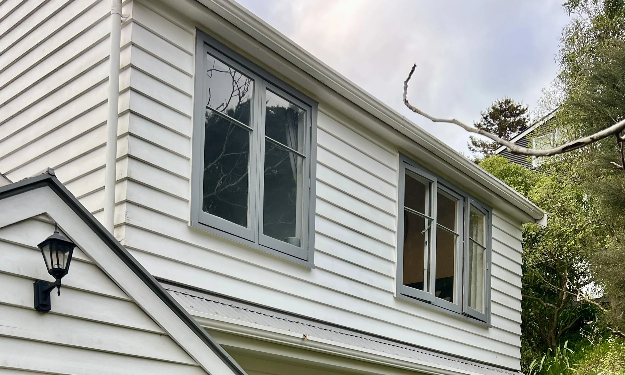 Photo of a white house with old timber joinery that will be removed and replaced with new double glazed and thermally broken aluminium joinery in Paraparaumu
