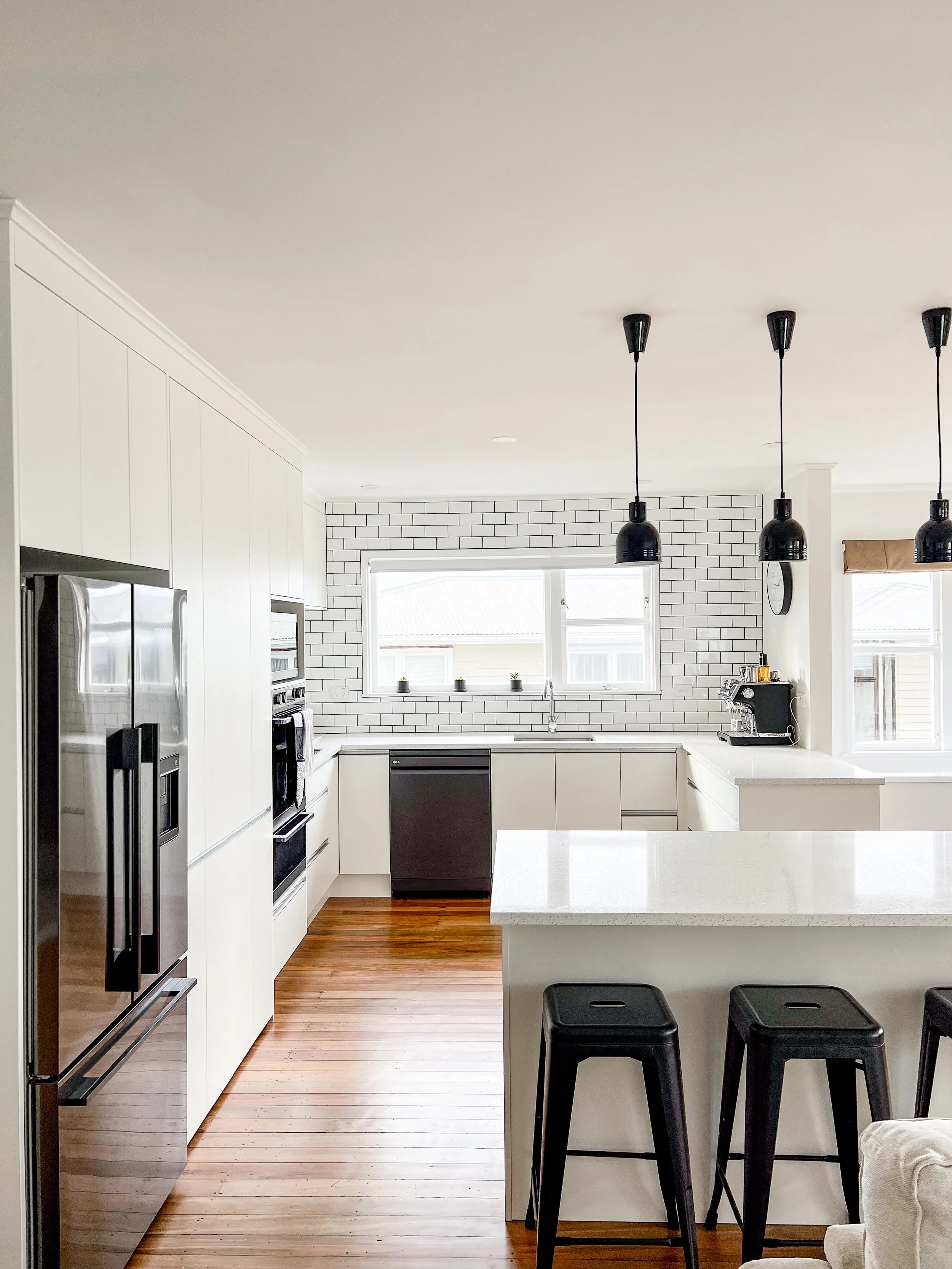 Modern kitchen in Johnsonville with white cabinetry, subway tile backsplash, black pendant lights, and hardwood flooring.