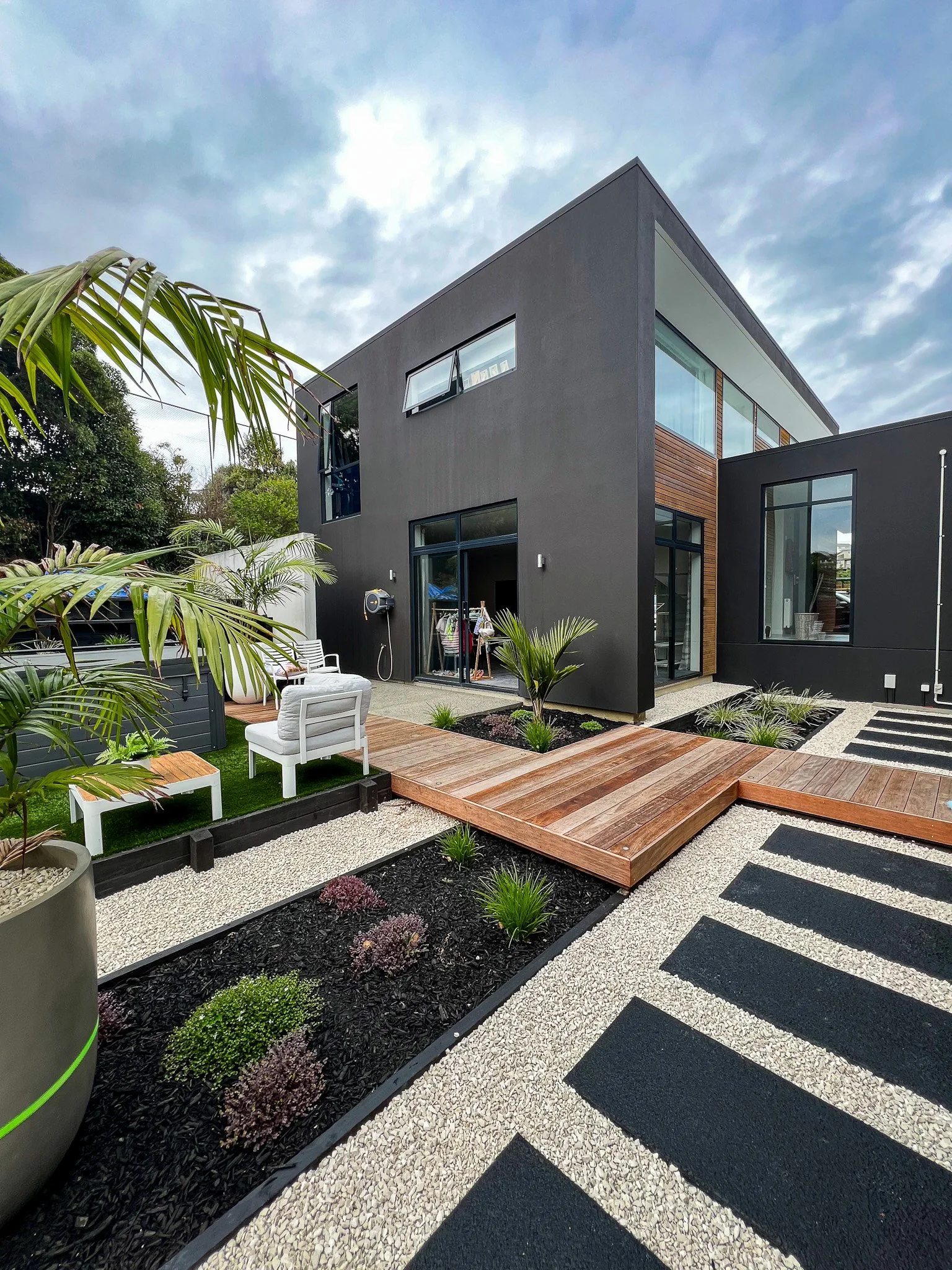 Modern two-story house with black exterior, large windows, and a landscaped backyard featuring a wooden deck, garden beds in Whitby