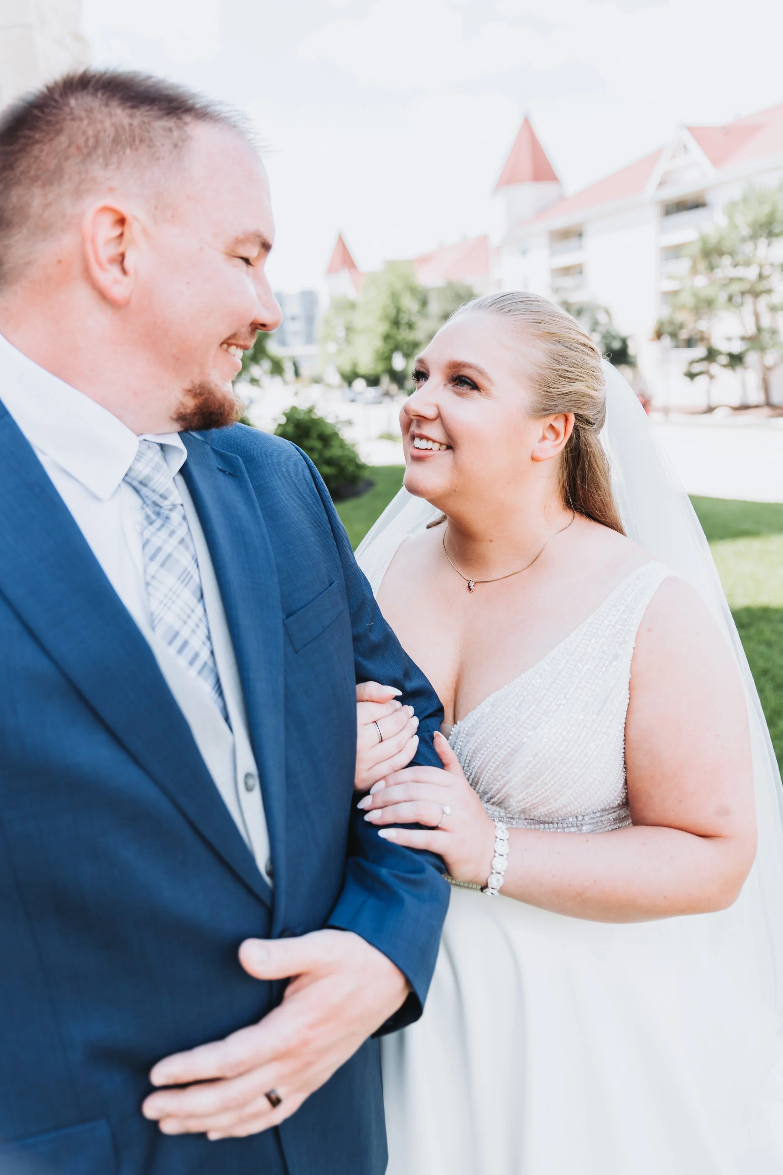 A bride and groom smiling and looking at each other outdoors during their wedding.