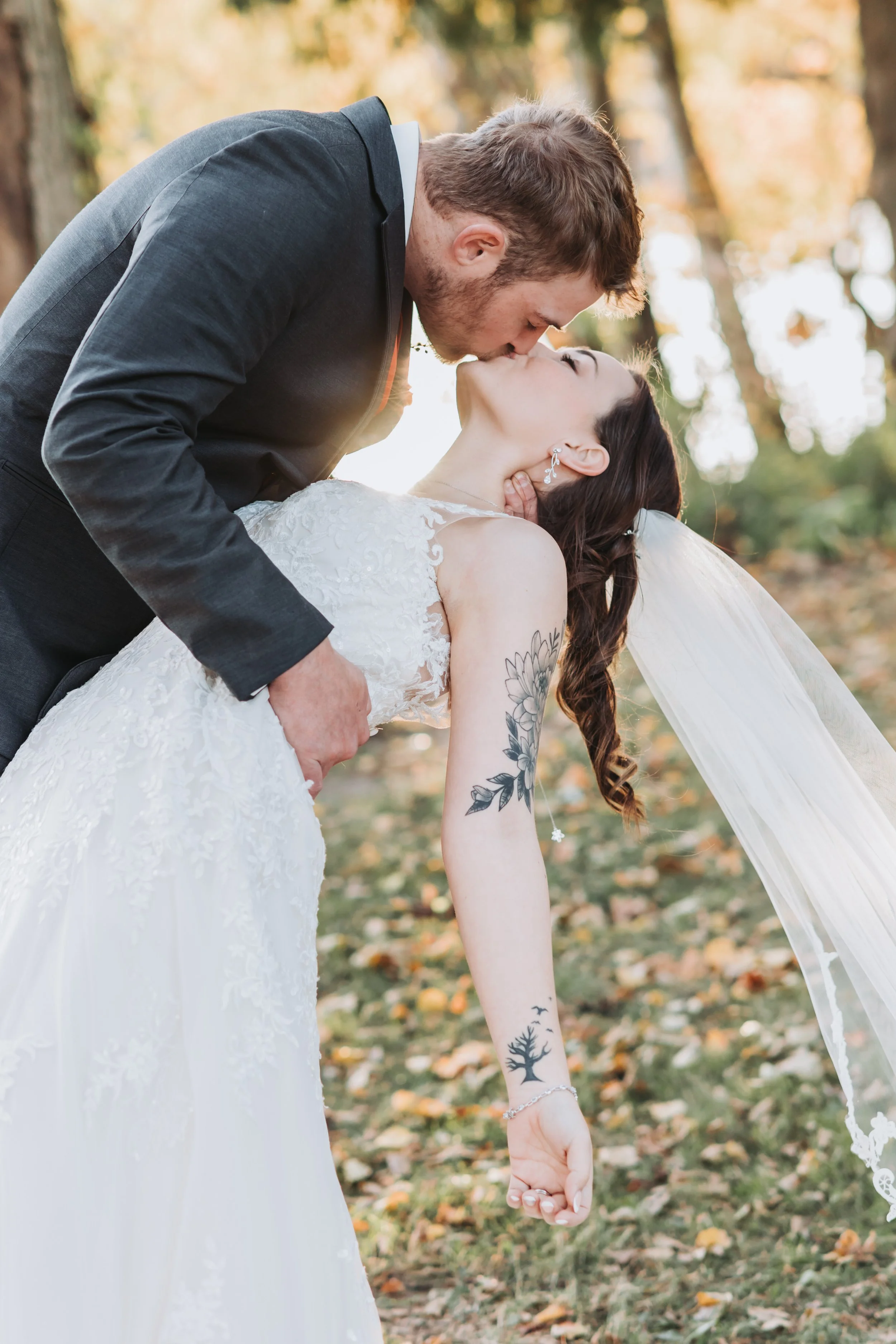 A bride and groom share a kiss outdoors during fall, with the groom dipping the bride backwards.