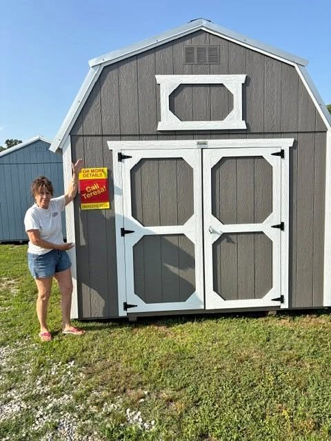 Woman standing next to a large outdoor storage shed with barn-style doors and a smaller windowed section at the peak of the roof.