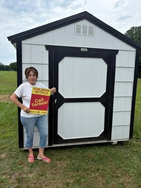 A woman standing beside a small shed holding a sign that says "For More Details Call Teresa! (804) 214-7628."
