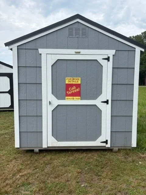 Gray storage shed with a white door and a yellow and red sign for more details and a phone number.