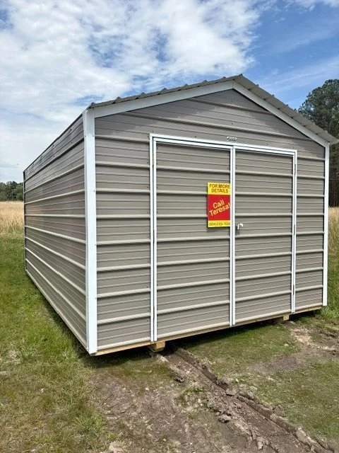A metal storage shed with a peaked roof, gray siding, and a sliding door displaying a sign for more details and a contact name.