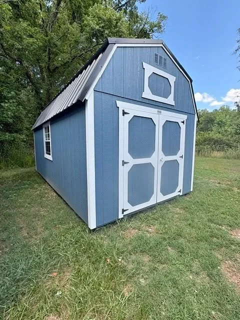 Blue outdoor storage shed with white trim, double doors, and small window, set on grass with trees in the background.