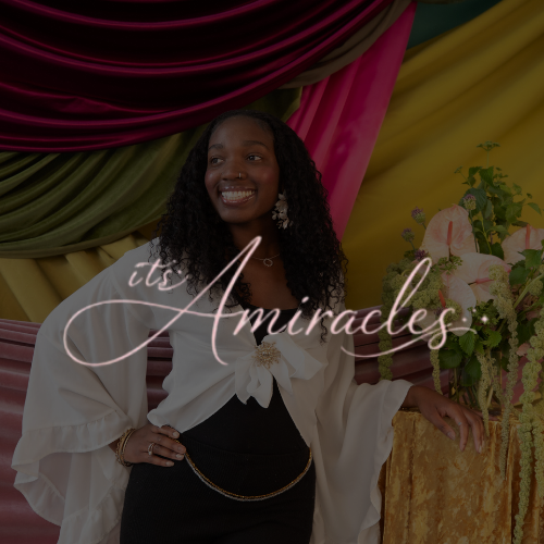 A smiling woman with long curly hair in front of colorful drapes and a floral arrangement, with the text "it's Miracles" overlayed.