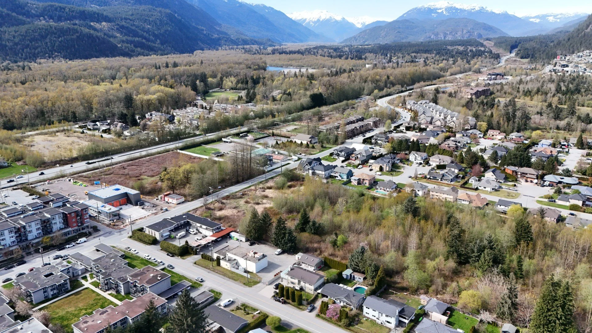 Aerial view of a suburban neighborhood surrounded by trees, mountains, and a river in the distance.