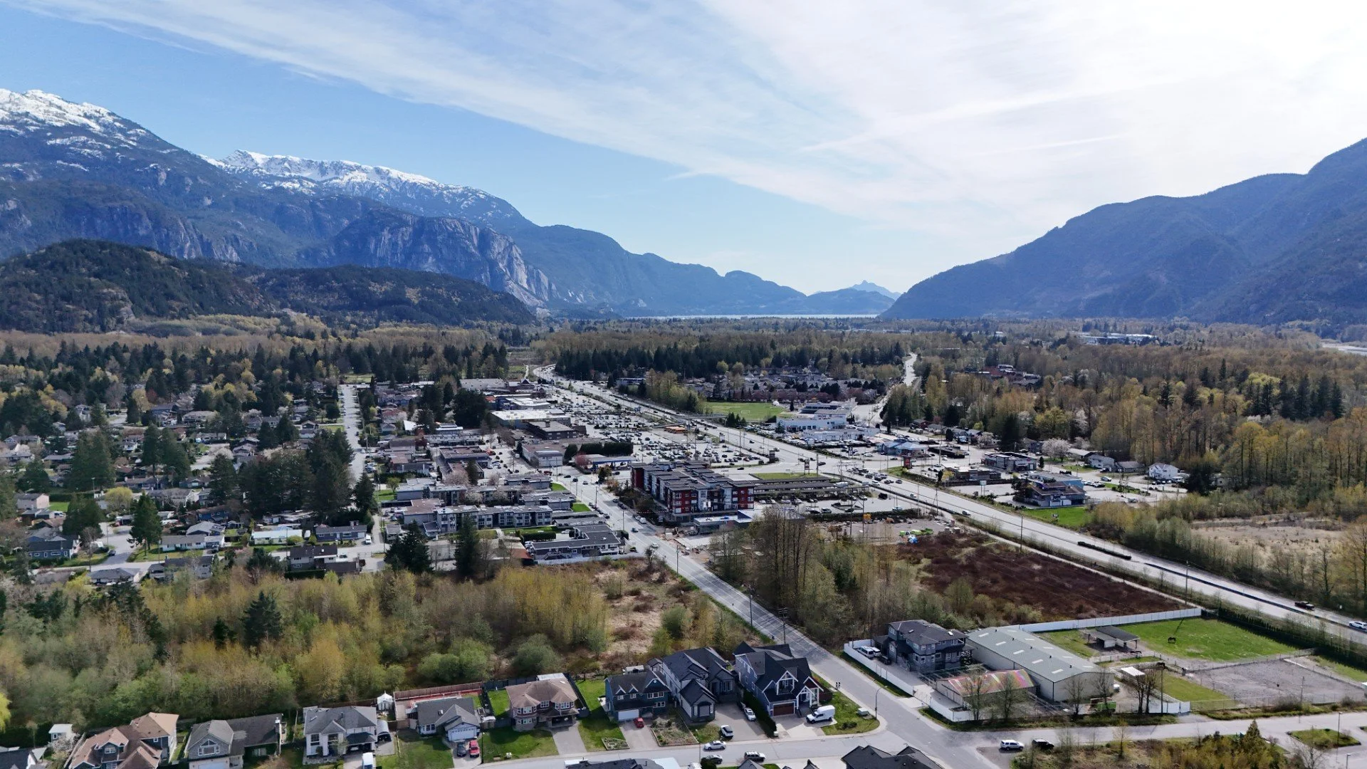 Aerial view of a town surrounded by mountains and greenery, with houses, commercial buildings, and roads.