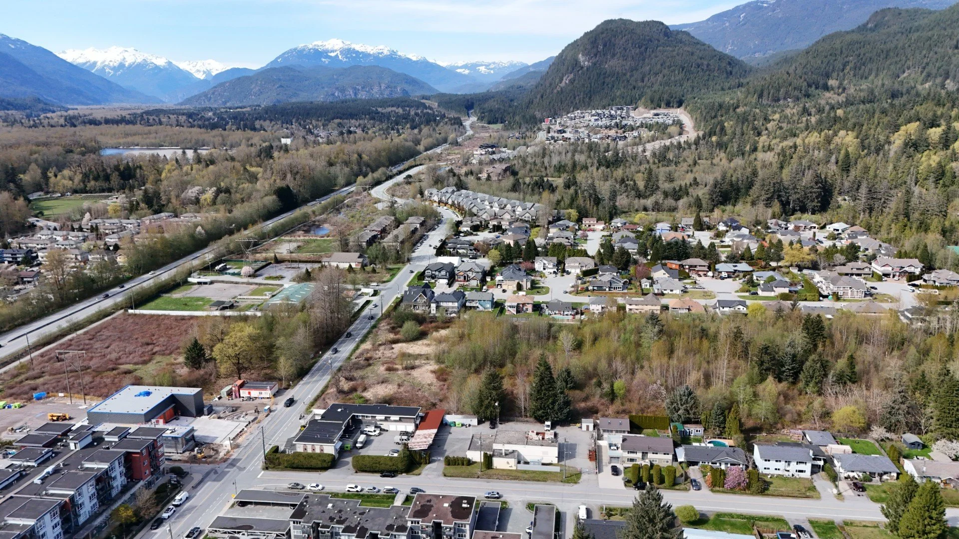 Aerial view of a small town surrounded by lush green trees and mountains with snow-capped peaks in the background.