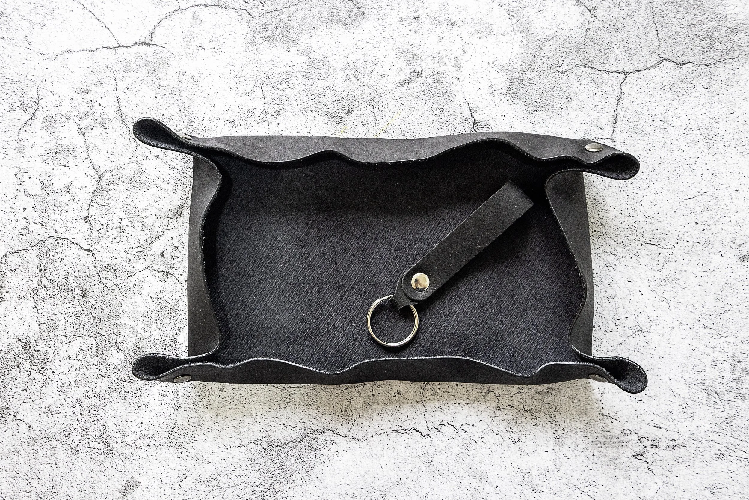 A black leather key holder with a ring inside, placed on a textured light gray surface.