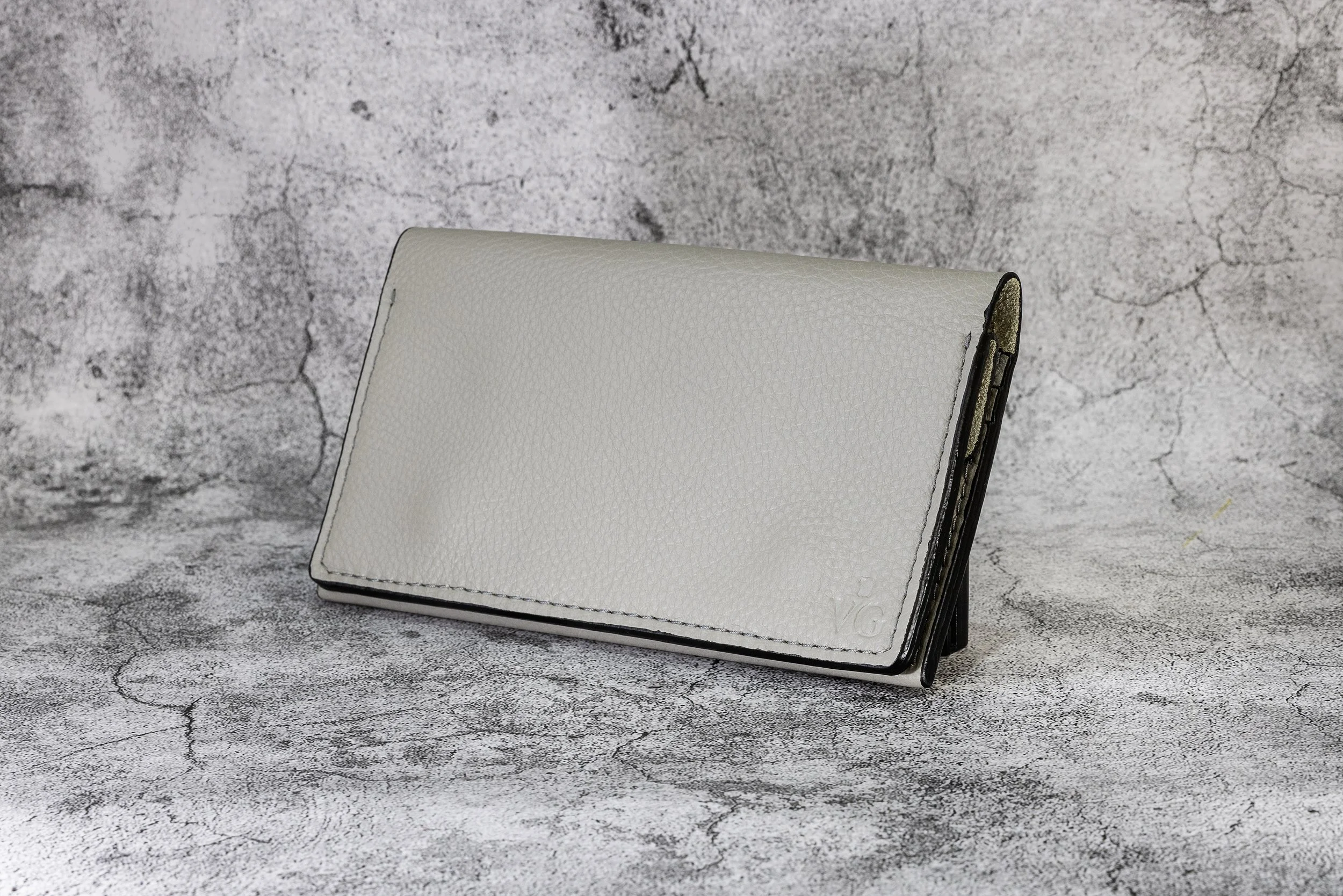 White leather wallet standing on a textured gray surface with a concrete wall background.