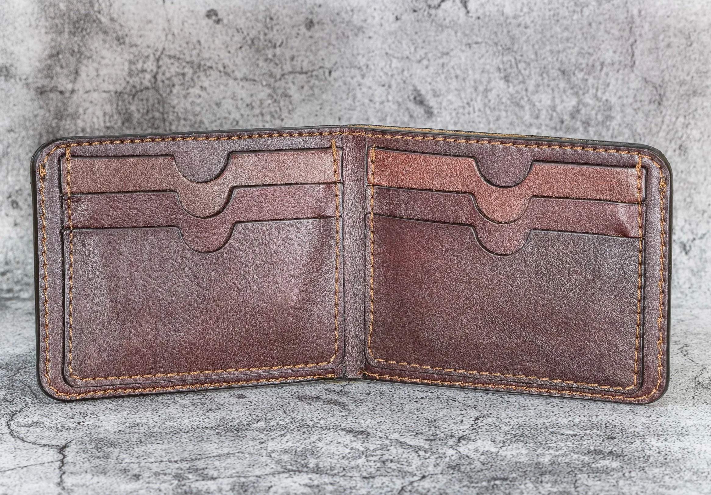 Open brown leather wallet with multiple card slots on a gray textured surface.