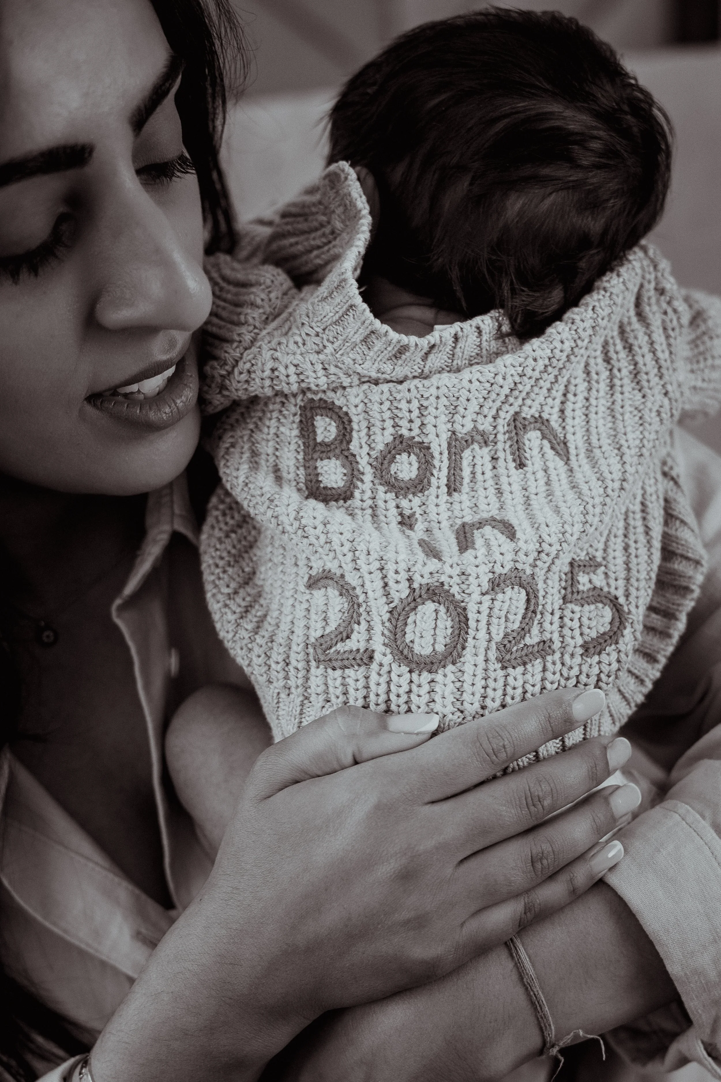 Mother holding new born son wearing a born in 2025 cardigan