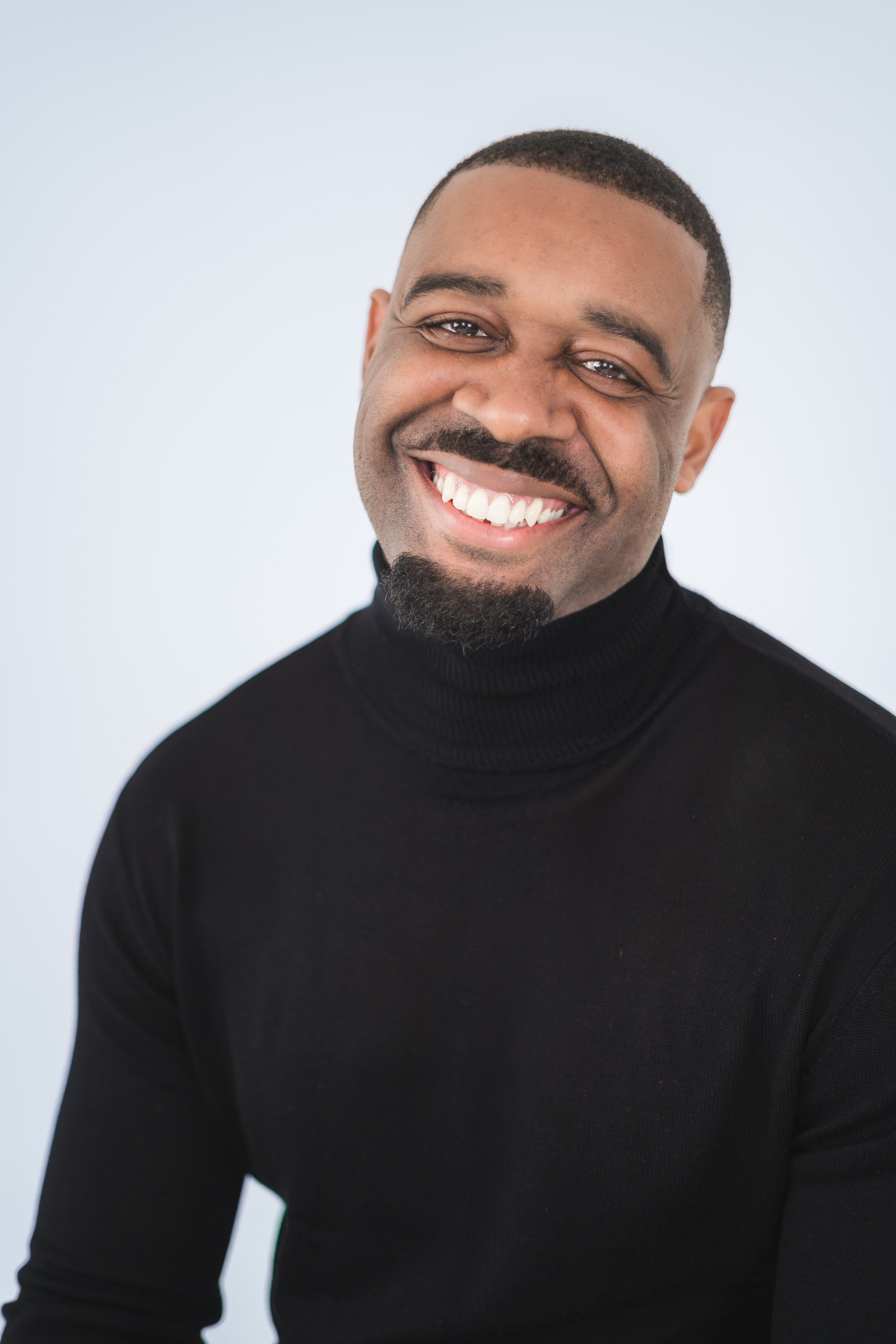 Smiling man wearing a black turtleneck against a light background.
