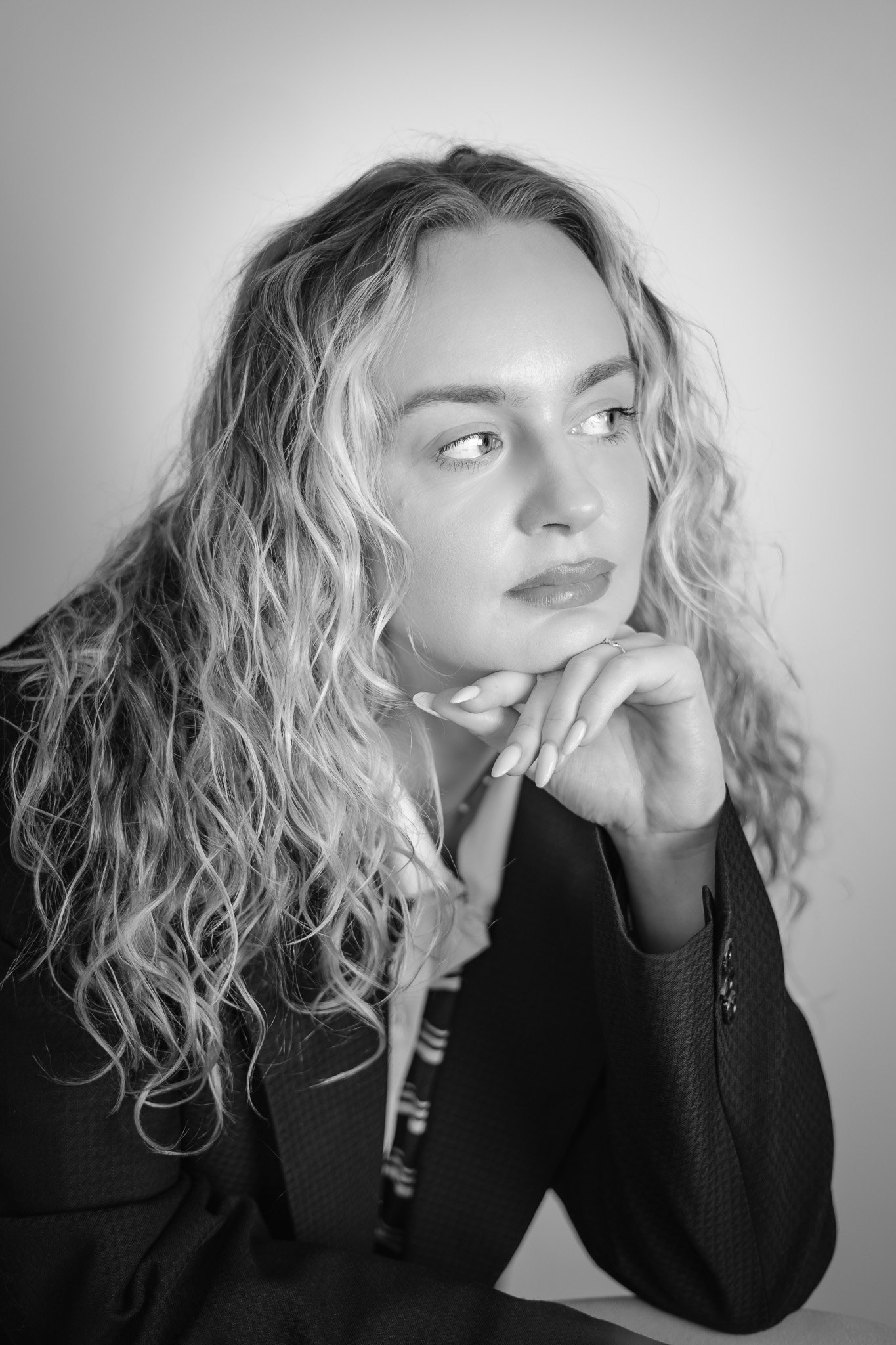 Black and white portrait of a woman with curly hair resting her chin on her hand, looking to the side.