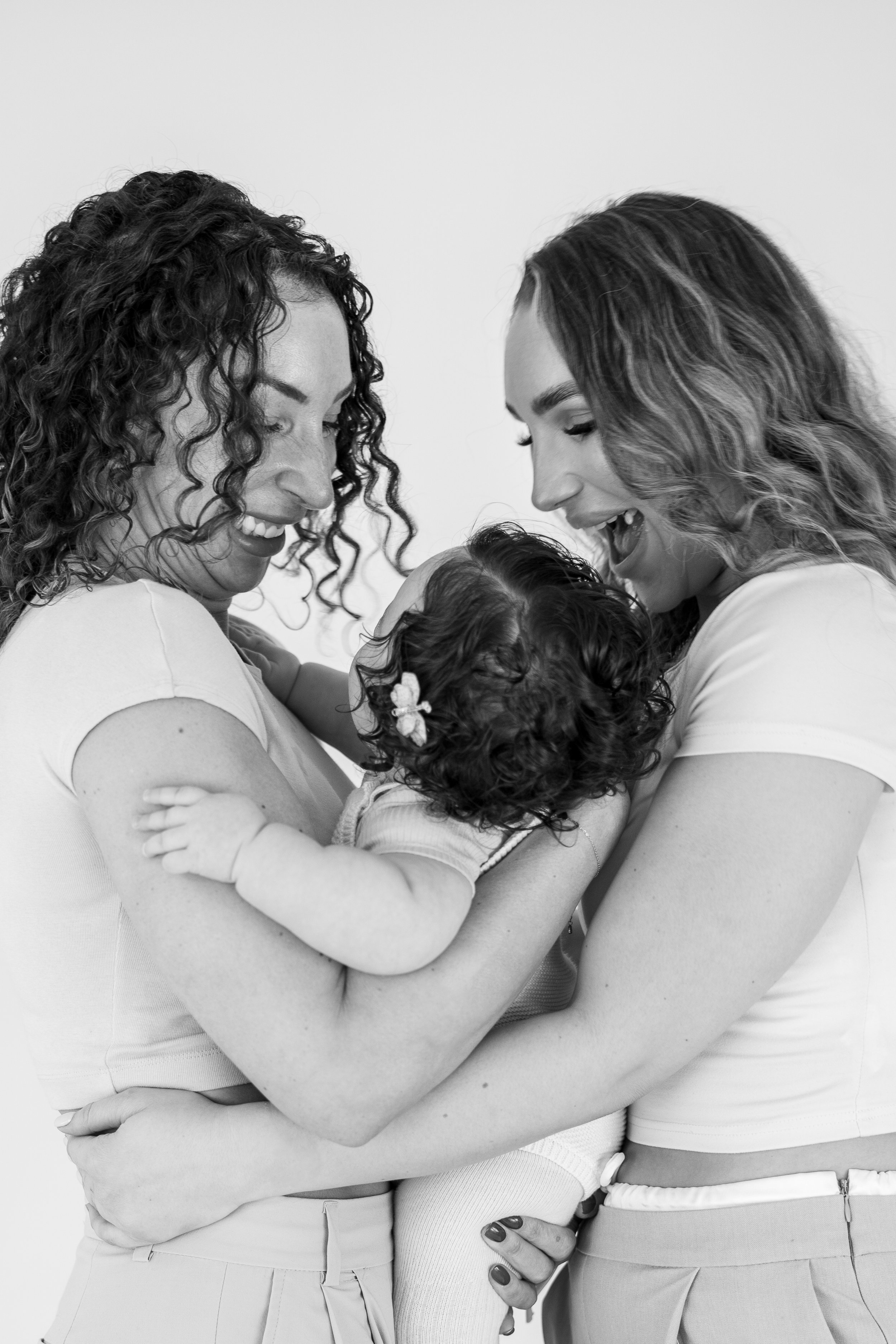 Two women and a young child smiling and holding each other in a black-and-white photo.
