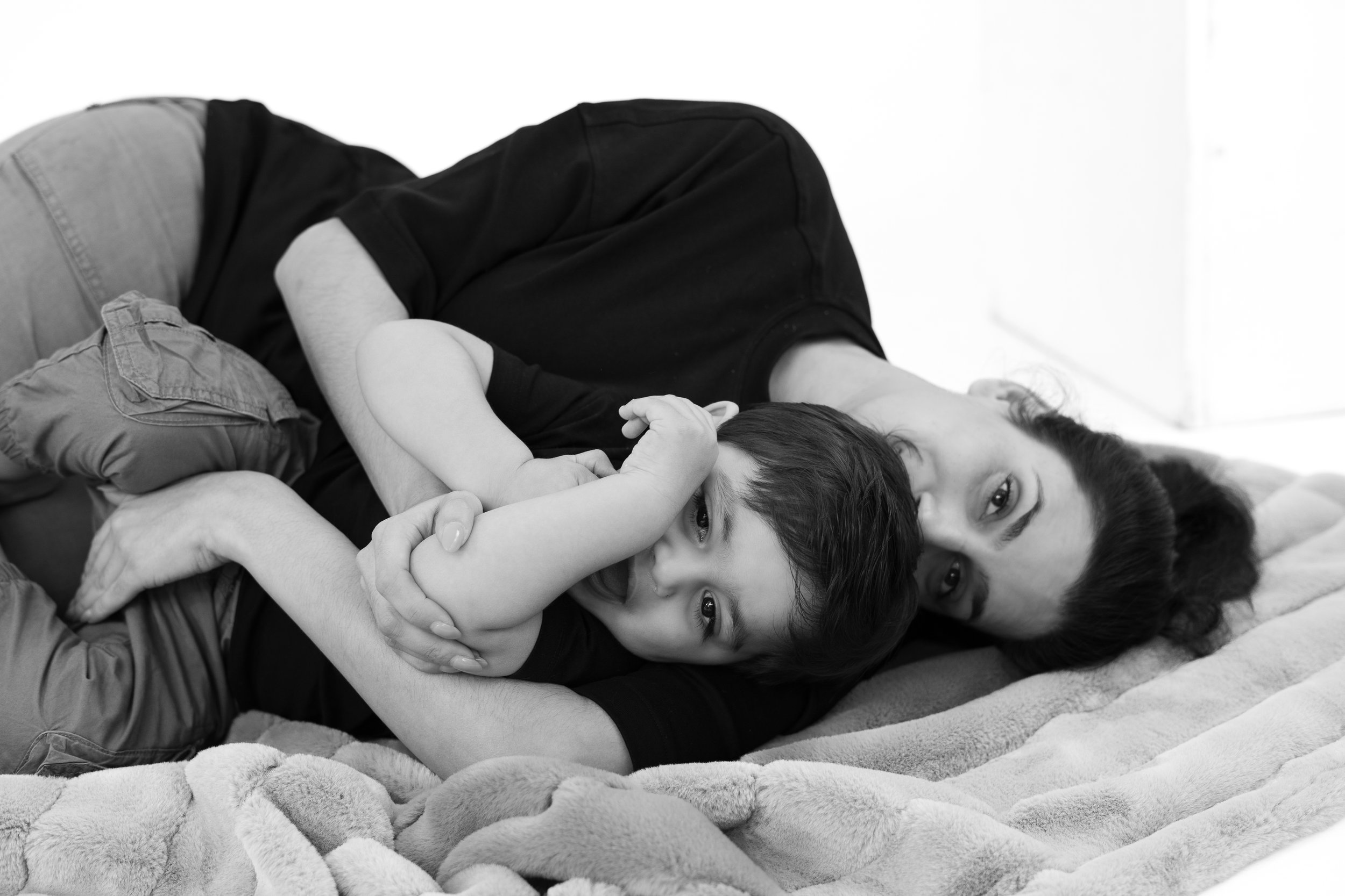 A woman and a young boy lying on a blanket, the boy playfully biting the woman's arm.