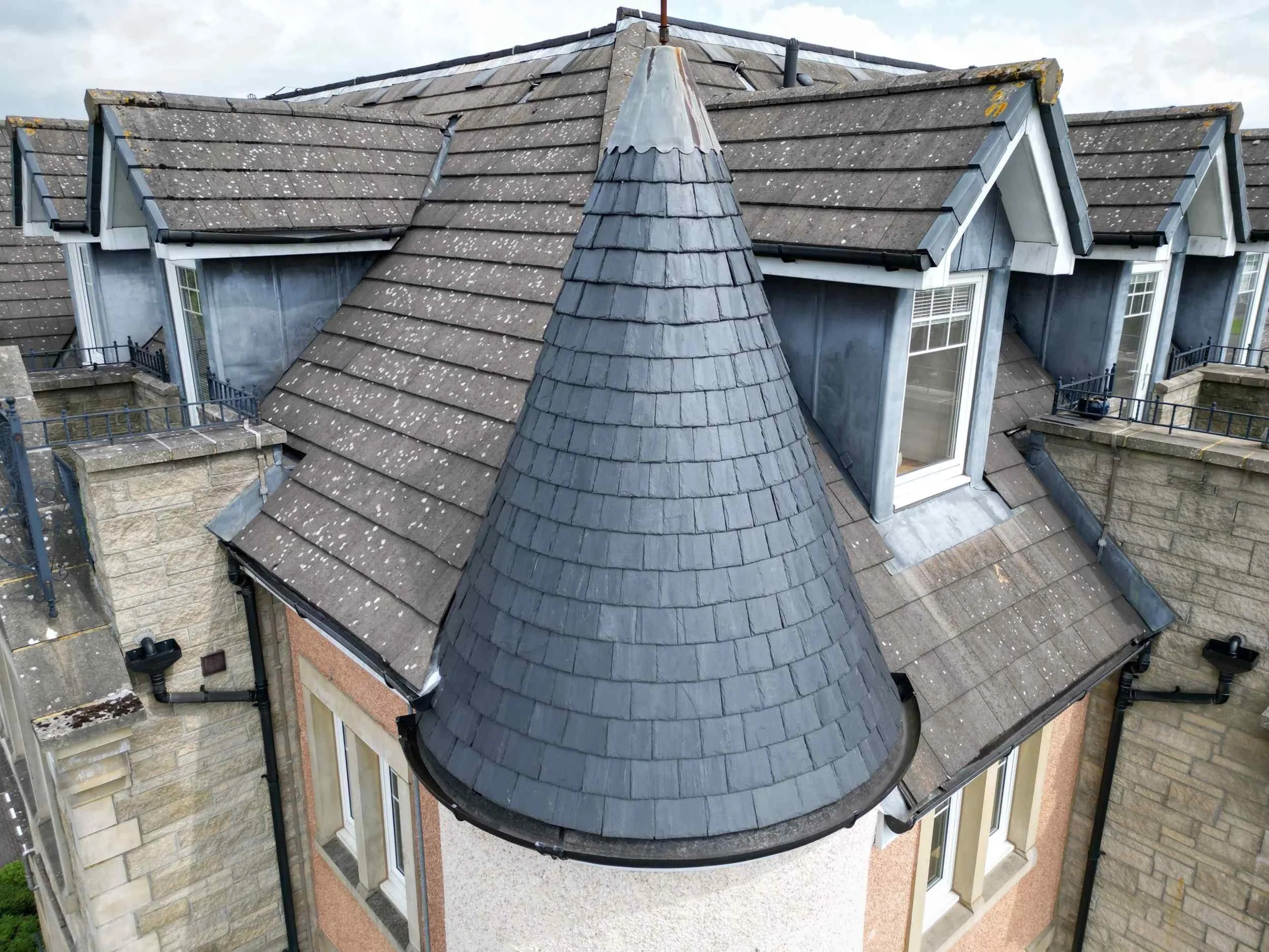Aerial view of a house with a tiled roof featuring multiple pitches, a rounded turret and dormer windows on the upper floors.