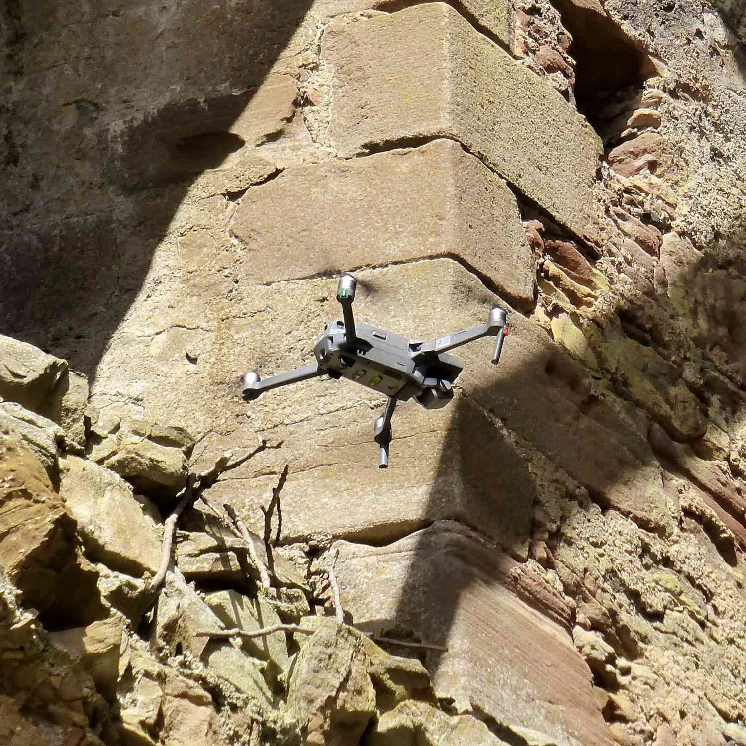 A drone flying near a rubble stone wall with sunlight illuminating part of the rocks.