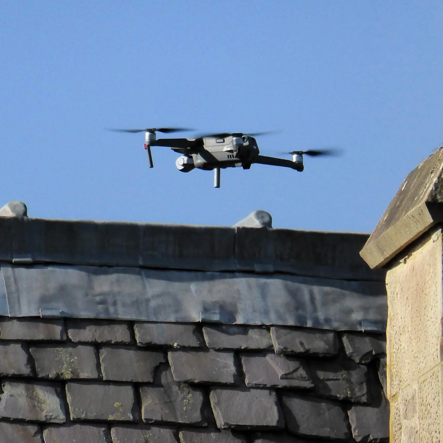Drone flying above a rooftop against a blue sky.