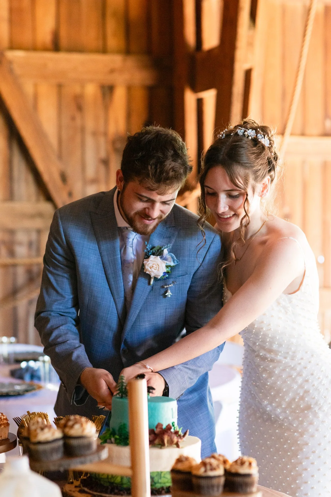 A bride and groom cutting a wedding cake in a wooden barn with warm lighting.