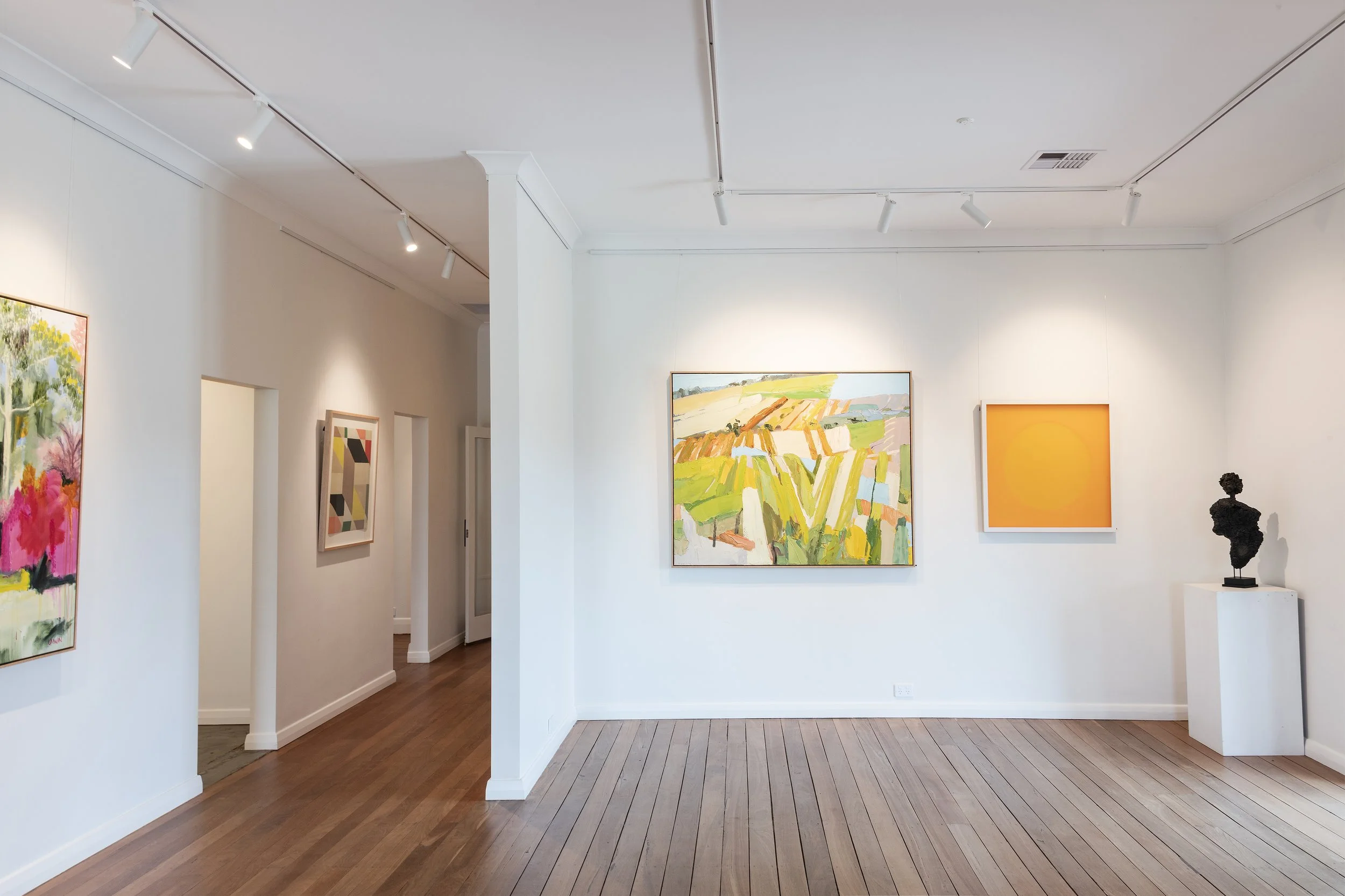 Interior view main gallery, with artworks by Lise Temple, Monika Morgenstern and Juliane Brandt with various colorful paintings on white walls and a black sculpture on a white pedestal, with wooden flooring.