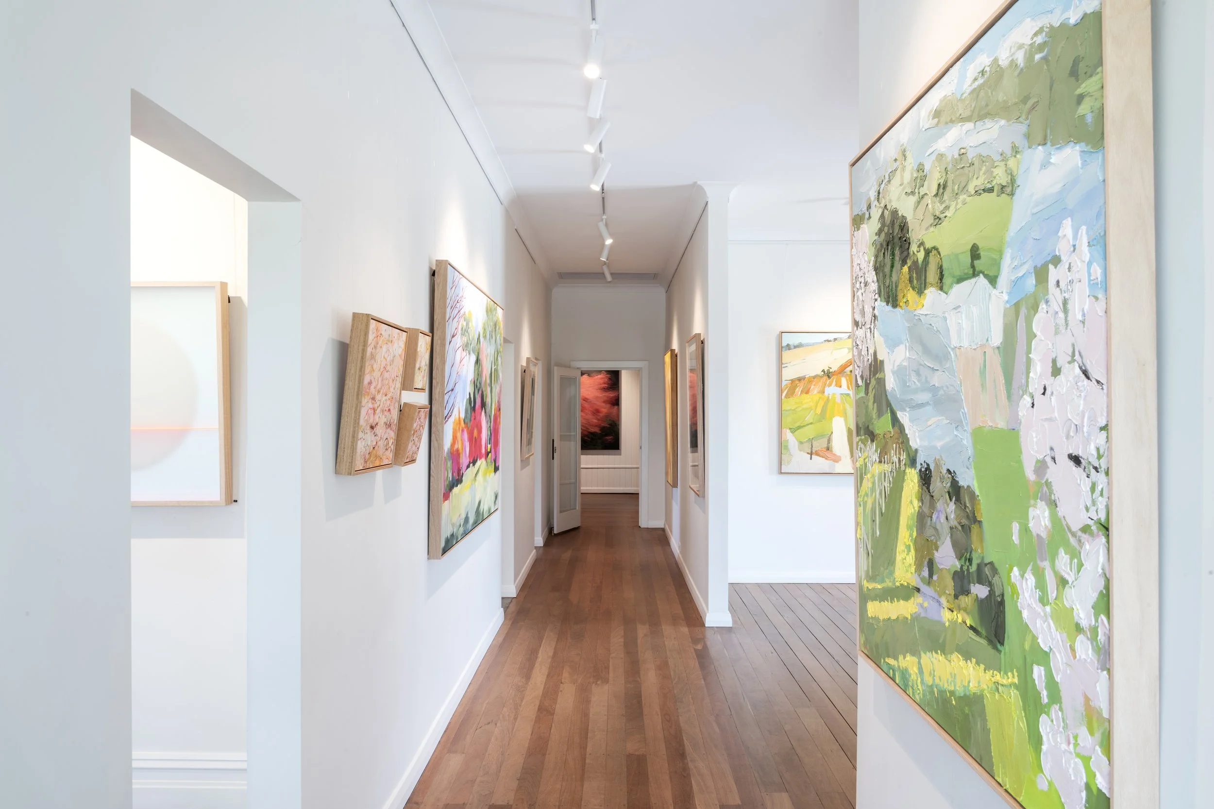 Art gallery hallway with artwork by Lise Temple, Sonya Unwin and Caroline Batchelor on white walls and wooden floors, leading to another exhibition space.