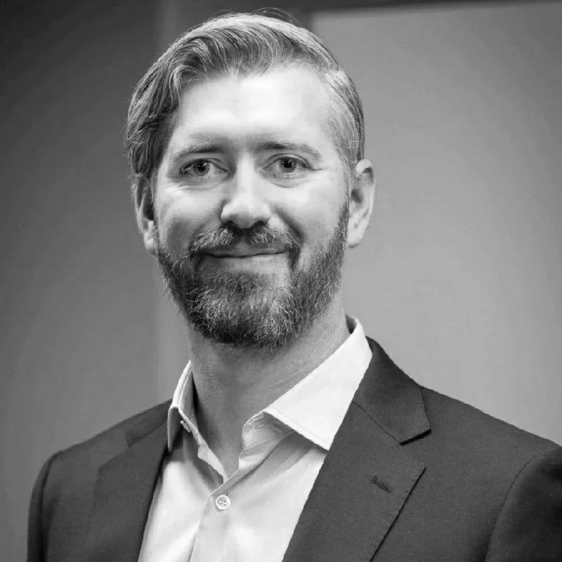 A professional headshot of Robert Brook, CAPDA Business Operations Manager, wearing a suit and collared shirt, against a plain background.