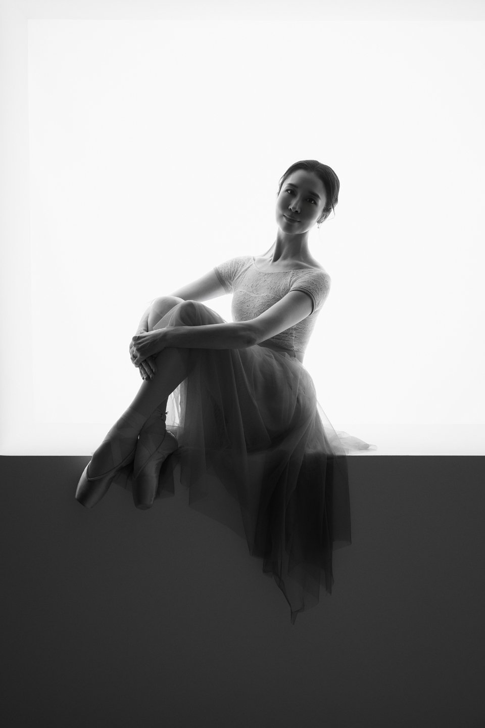 Black-and-white seated ballet portrait of Julie beside a window.